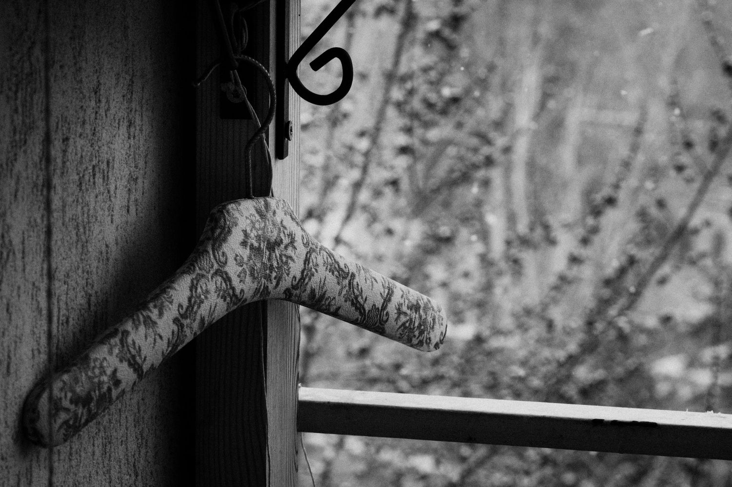 Rustic wooden coat hanger mounted on dark wall with winter scene visible through window.