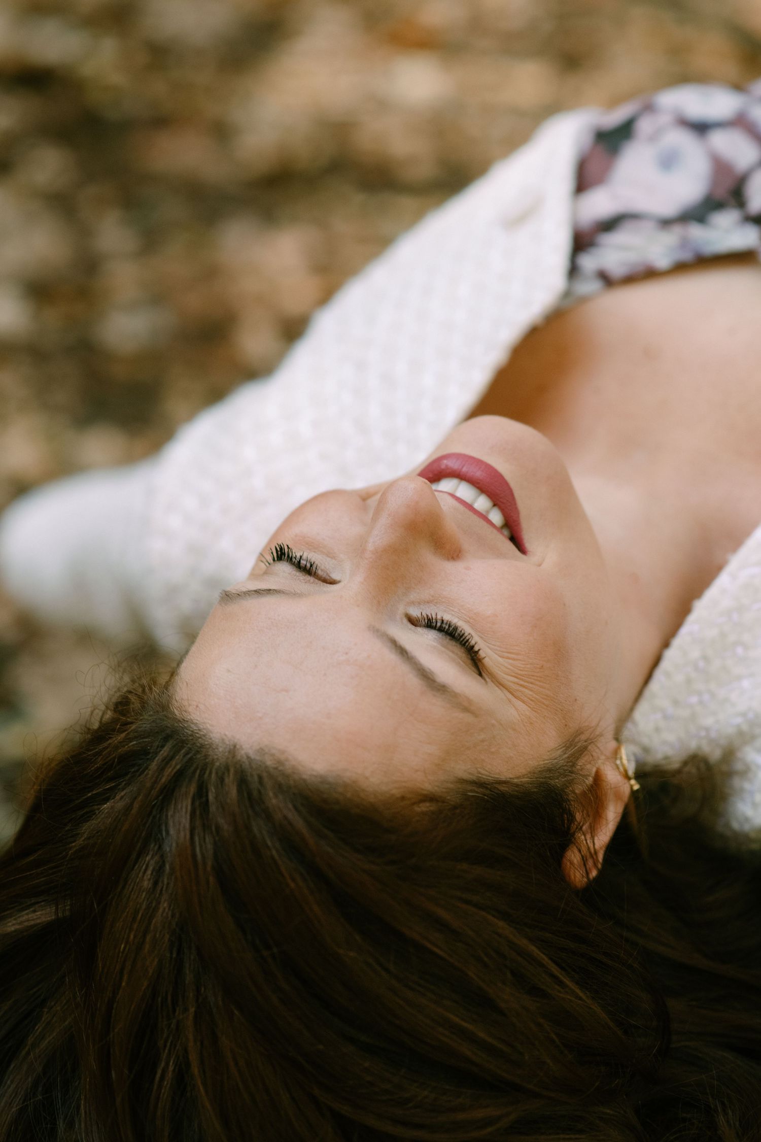 Dark-haired figure lying down with a joyful smile and closed eyes in natural light.