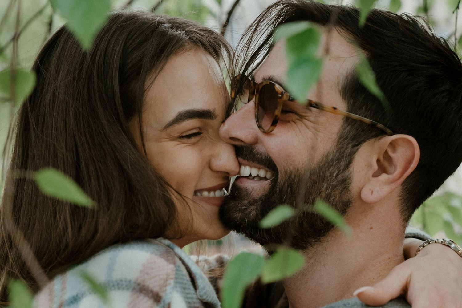 Intimate close-up portrait of a couple sharing a playful moment among green foliage.