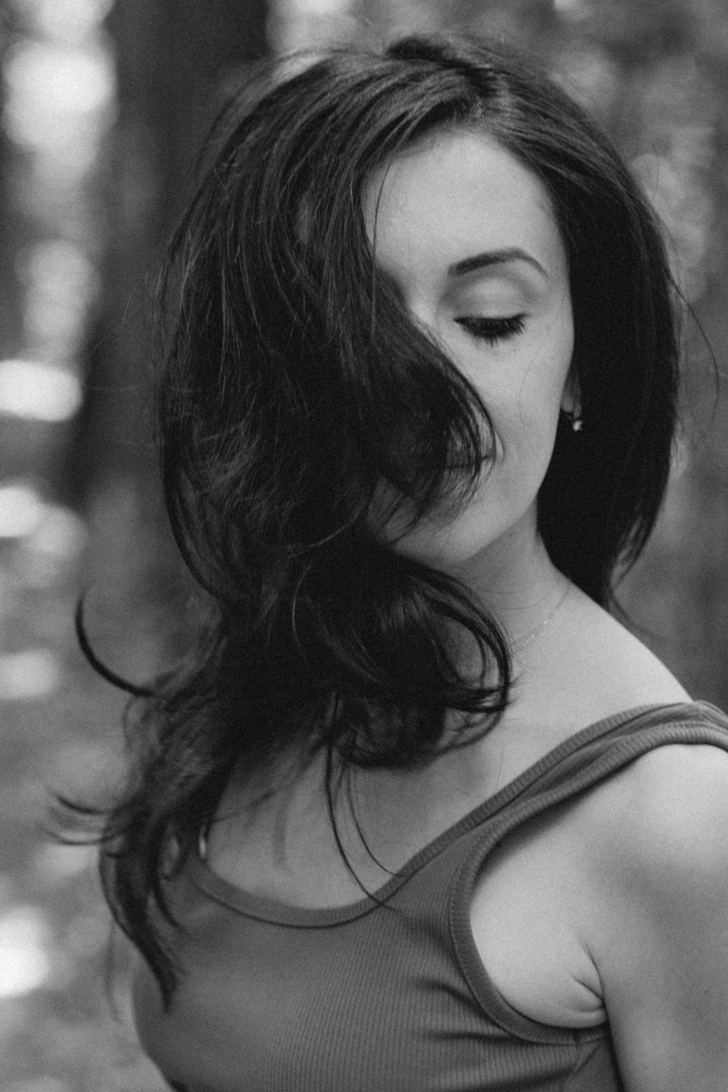 Black and white portrait showing dark hair flowing in the wind against a soft blurred background.