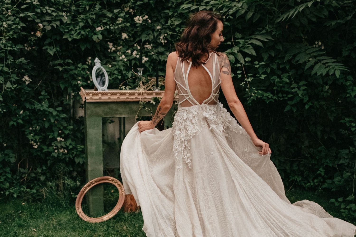 Bride in flowing lace back wedding dress twirling in garden setting.