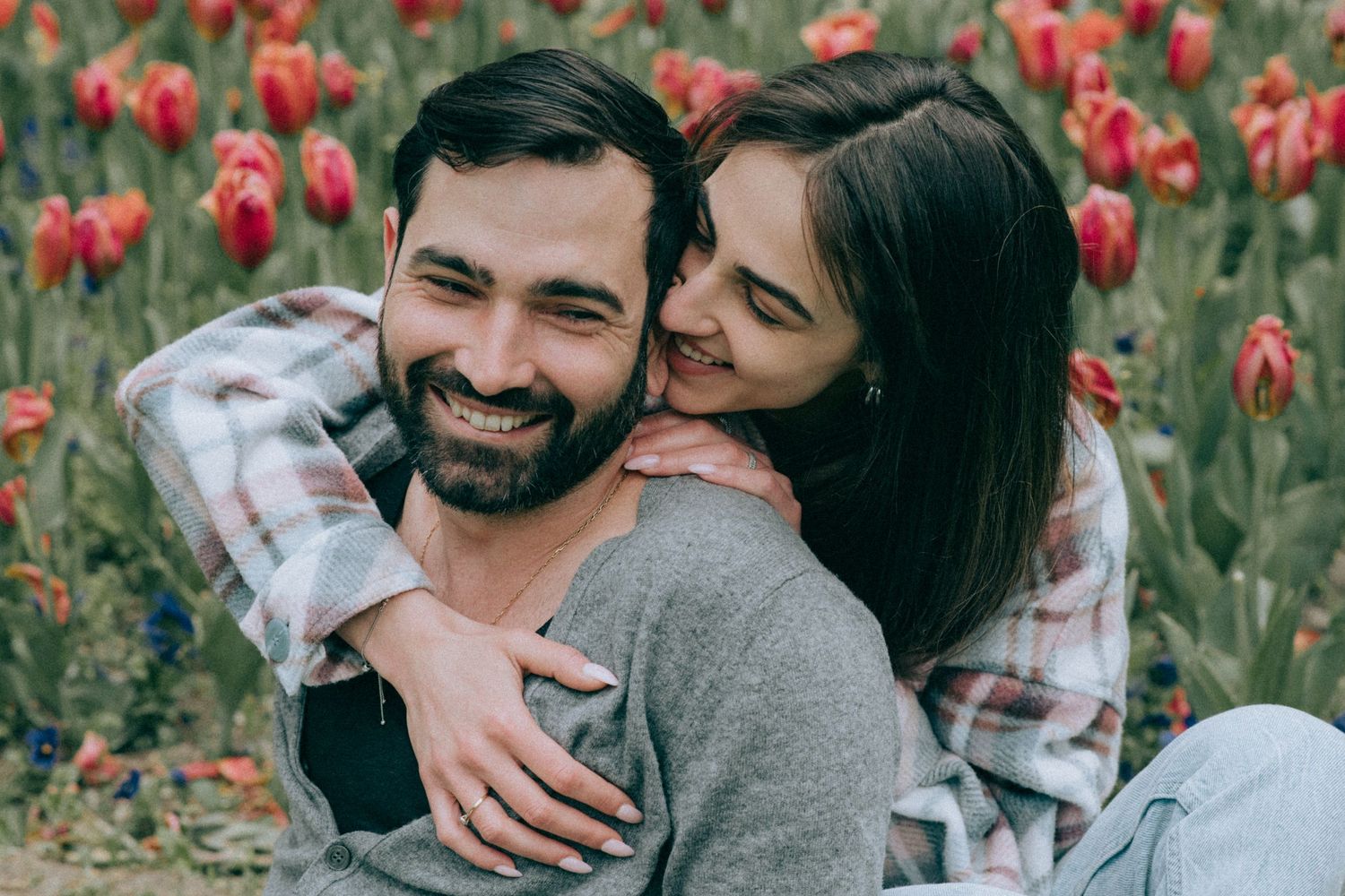 Happy couple laughing together in a field of red tulips.