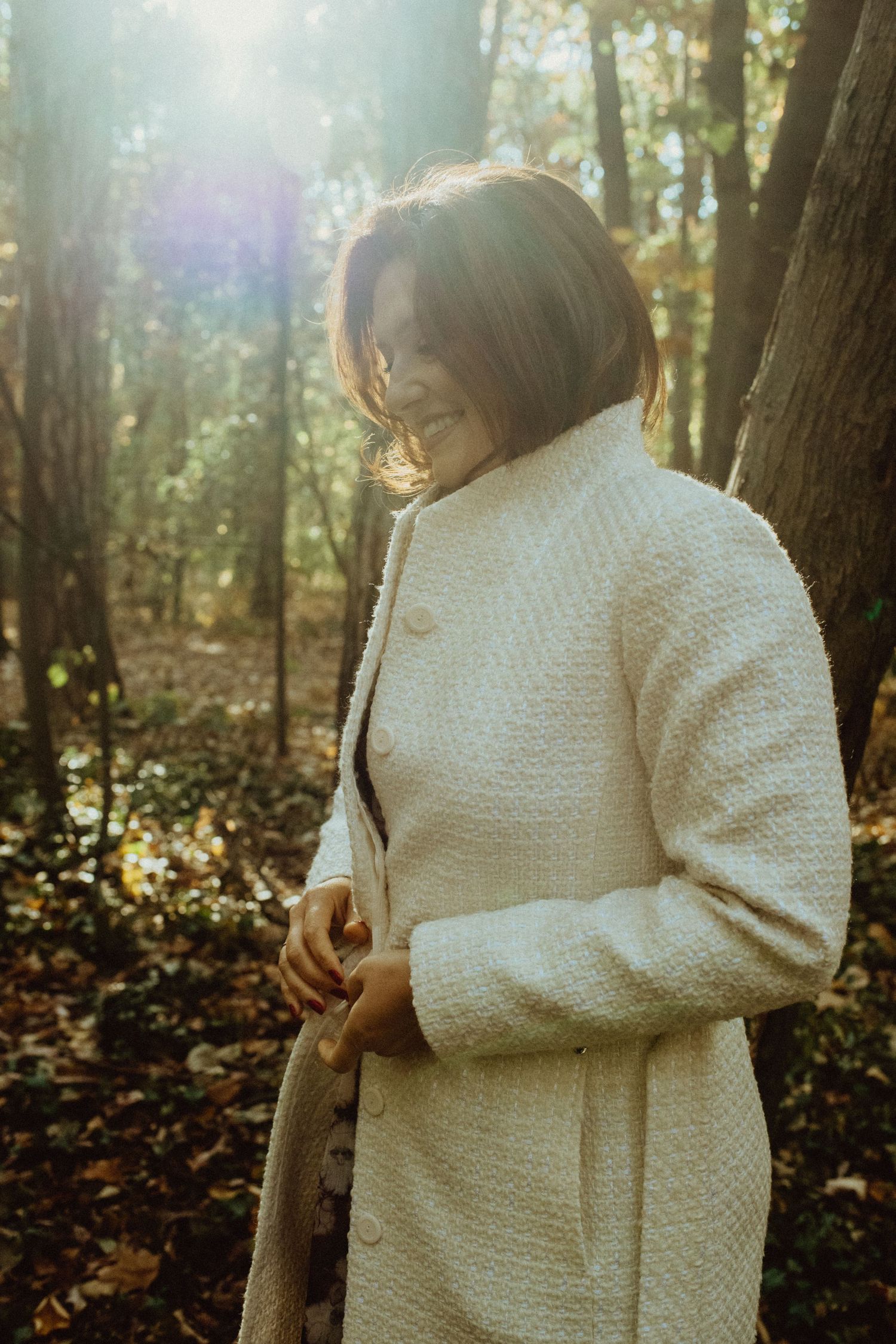 Person in white knit sweater holding walking stick in sunlit forest.