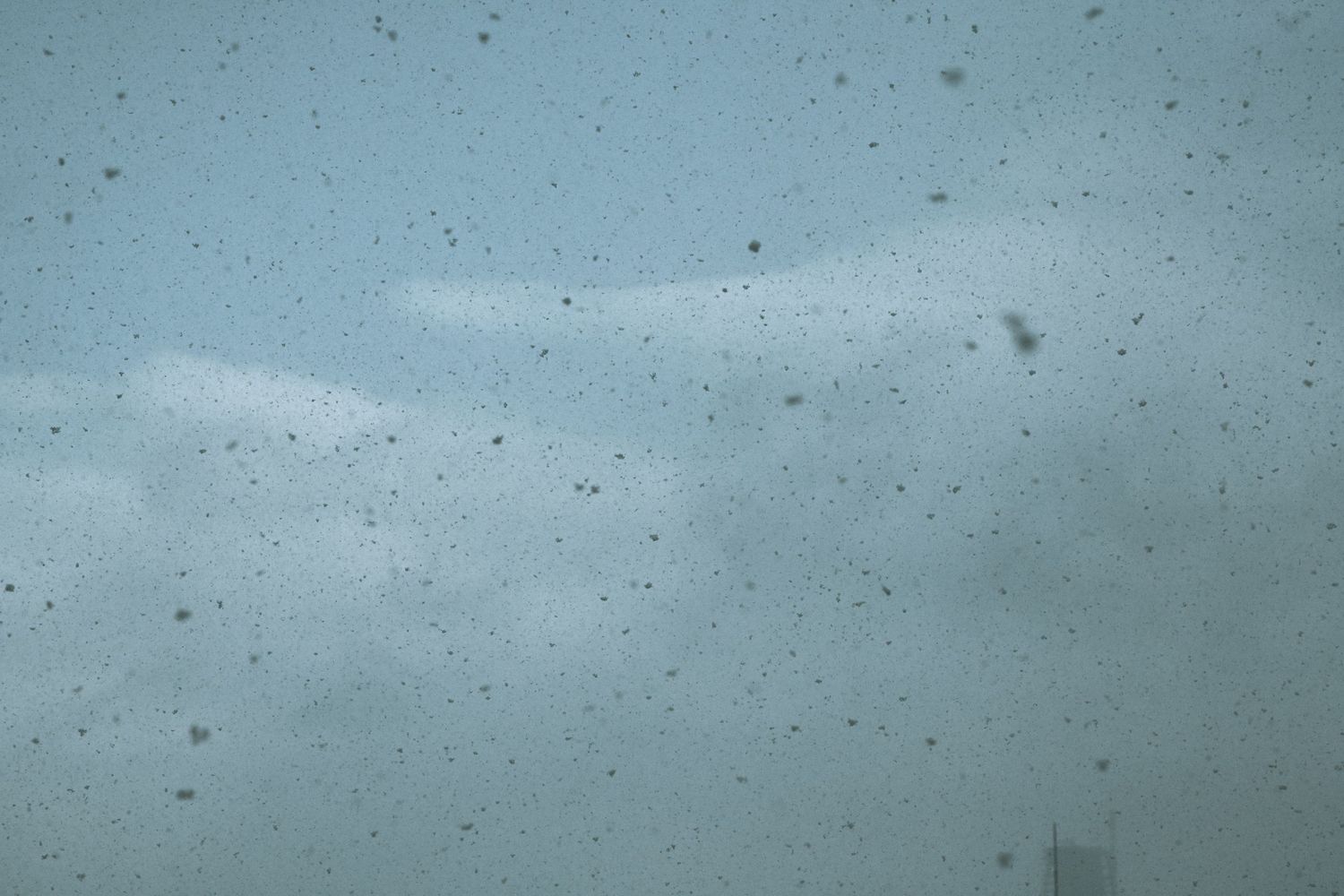 Raindrops or water droplets on glass window against cloudy sky.
