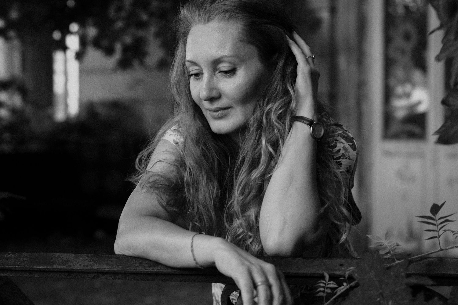Black and white portrait of person with long wavy hair resting against railing.