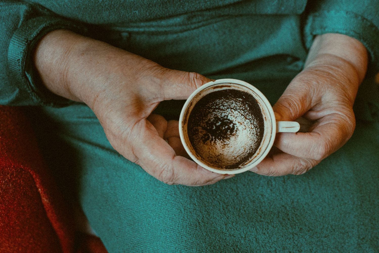 Person holding and sifting dry coffee grounds through a metal filter over a ceramic mug.