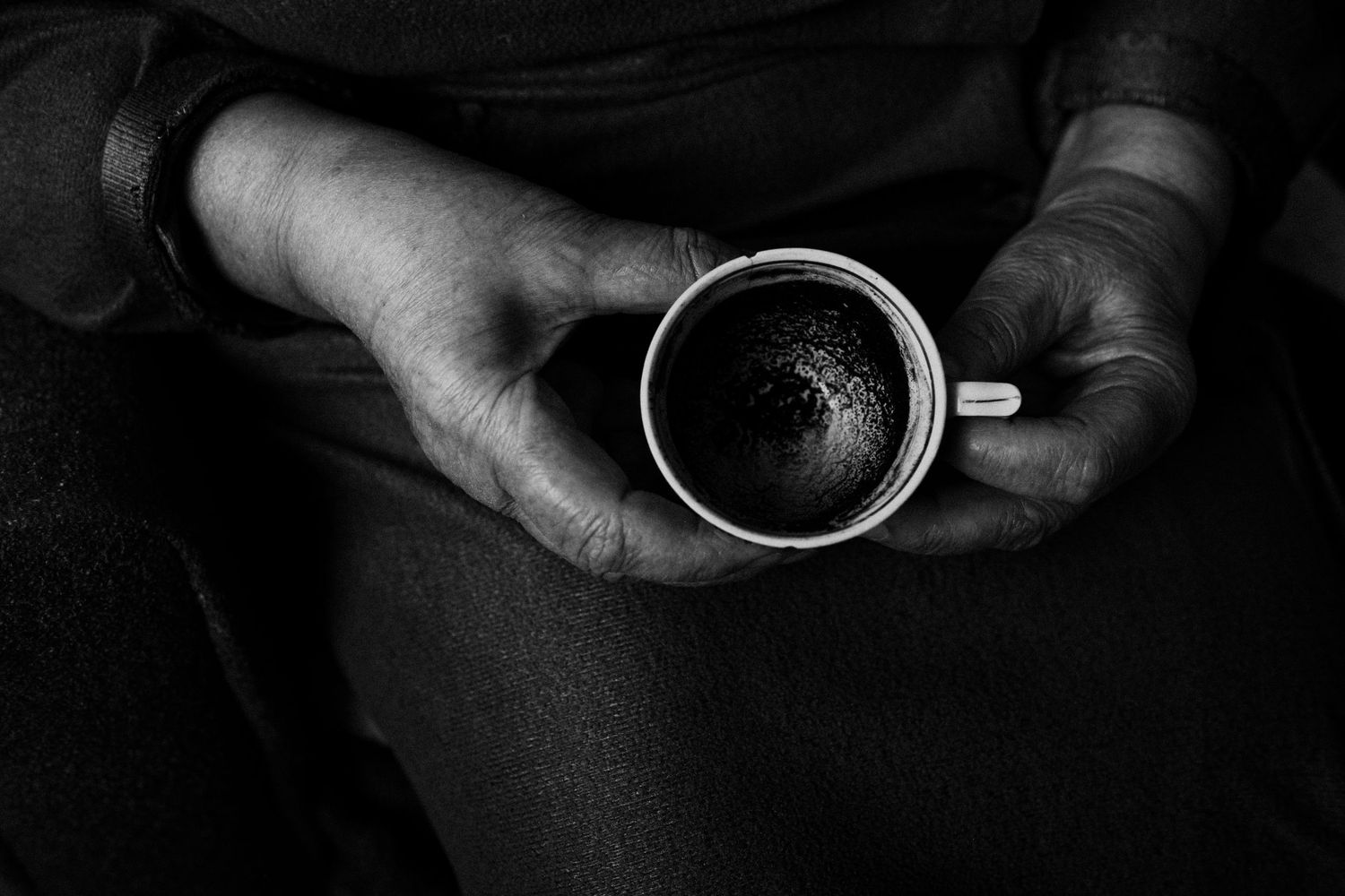 Overhead view of hands holding a black coffee cup against dark background.