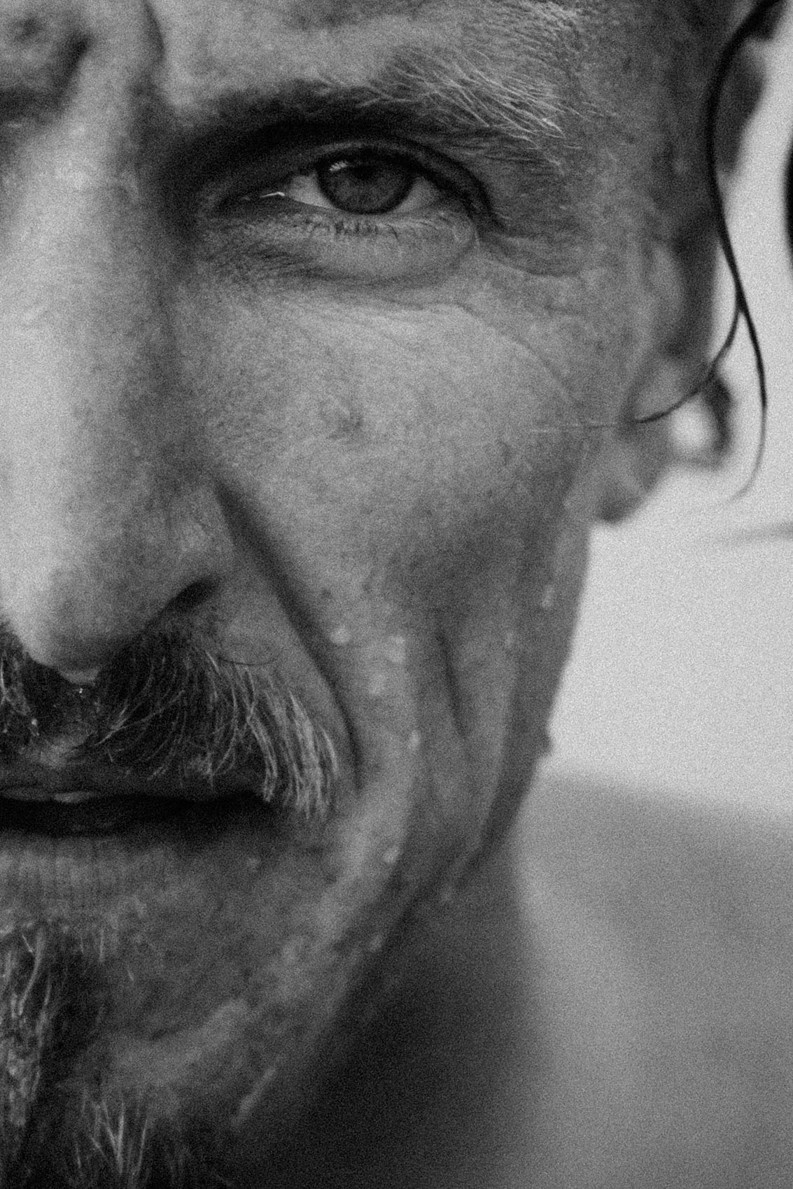 Close up black and white portrait showing half of a bearded man's smiling face.