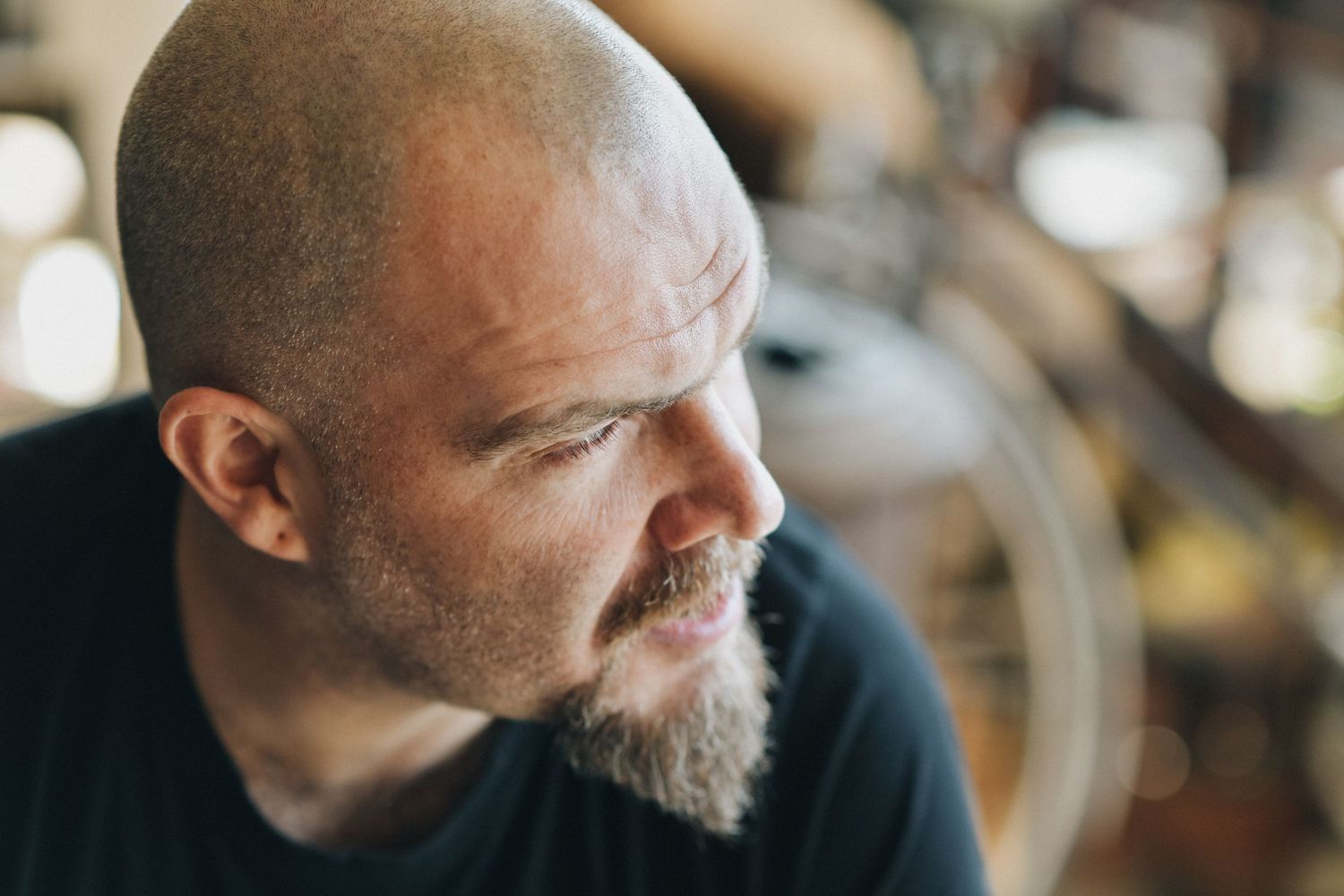 A contemplative side profile portrait of a person with a bald head and beard in soft lighting.