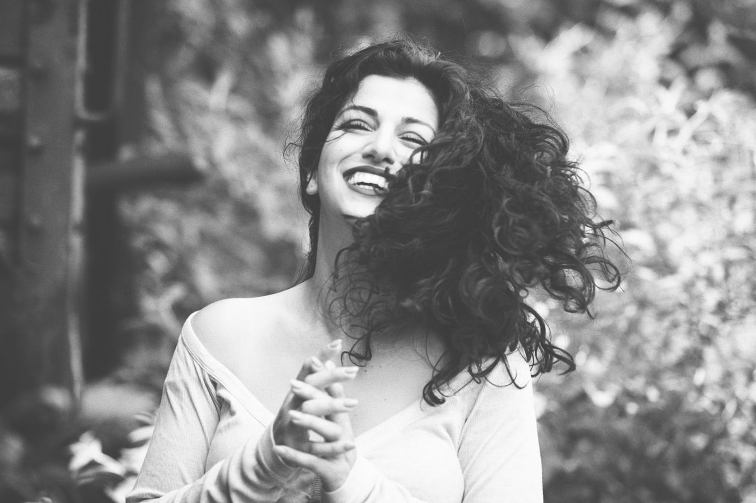 A black and white photo collage showing a person with curly hair outdoors smiling and striking different playful poses.