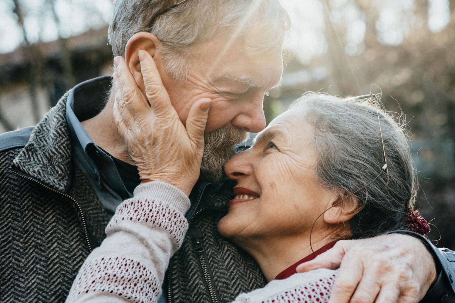 Tender moment between elderly couple sharing an intimate embrace outdoors.