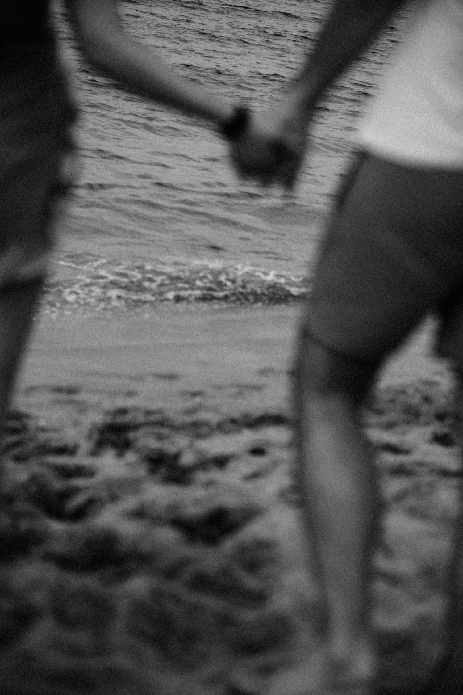 Black and white image of hands holding by the ocean shore.