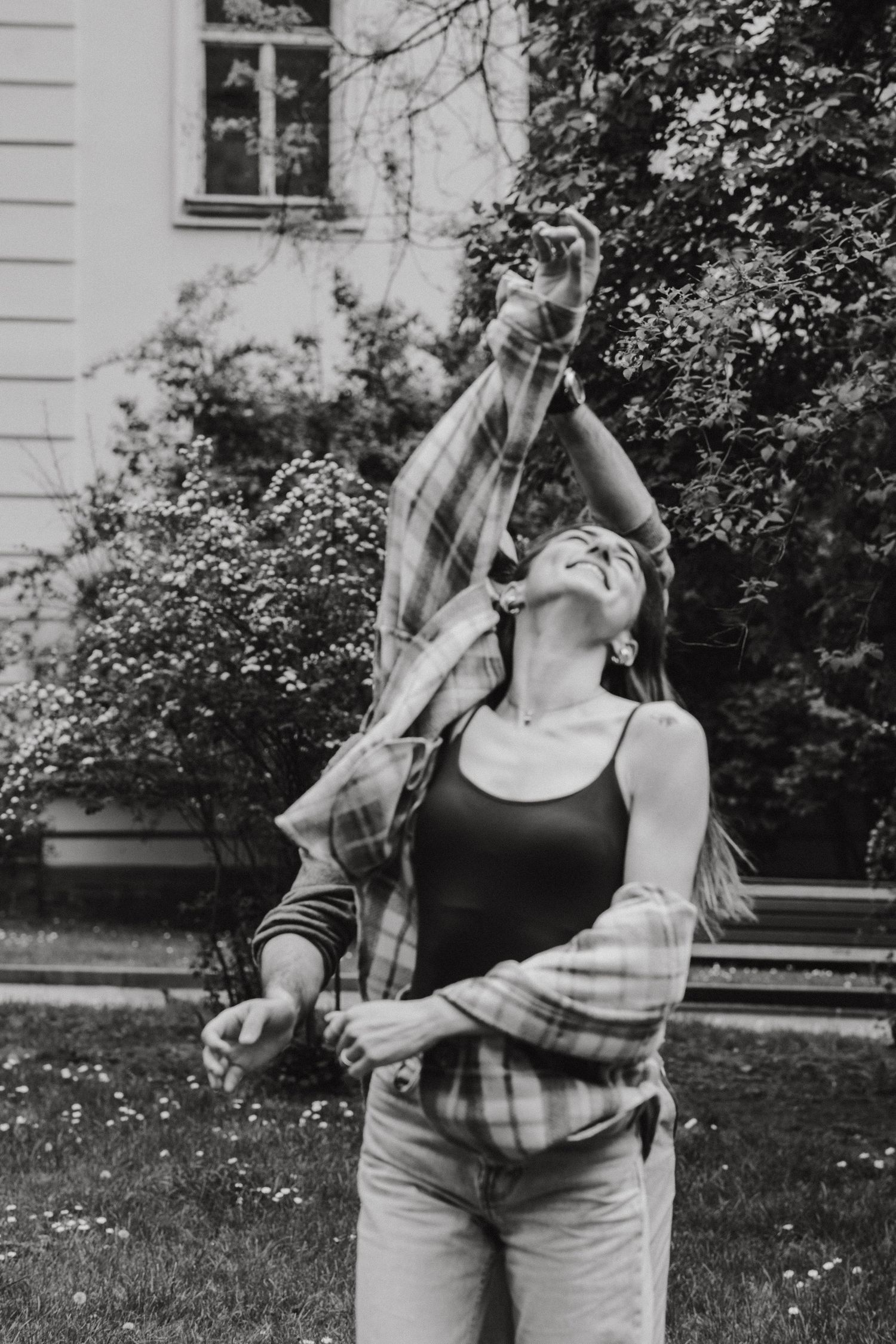 Black and white photo of someone dancing joyfully in casual clothes outdoors.