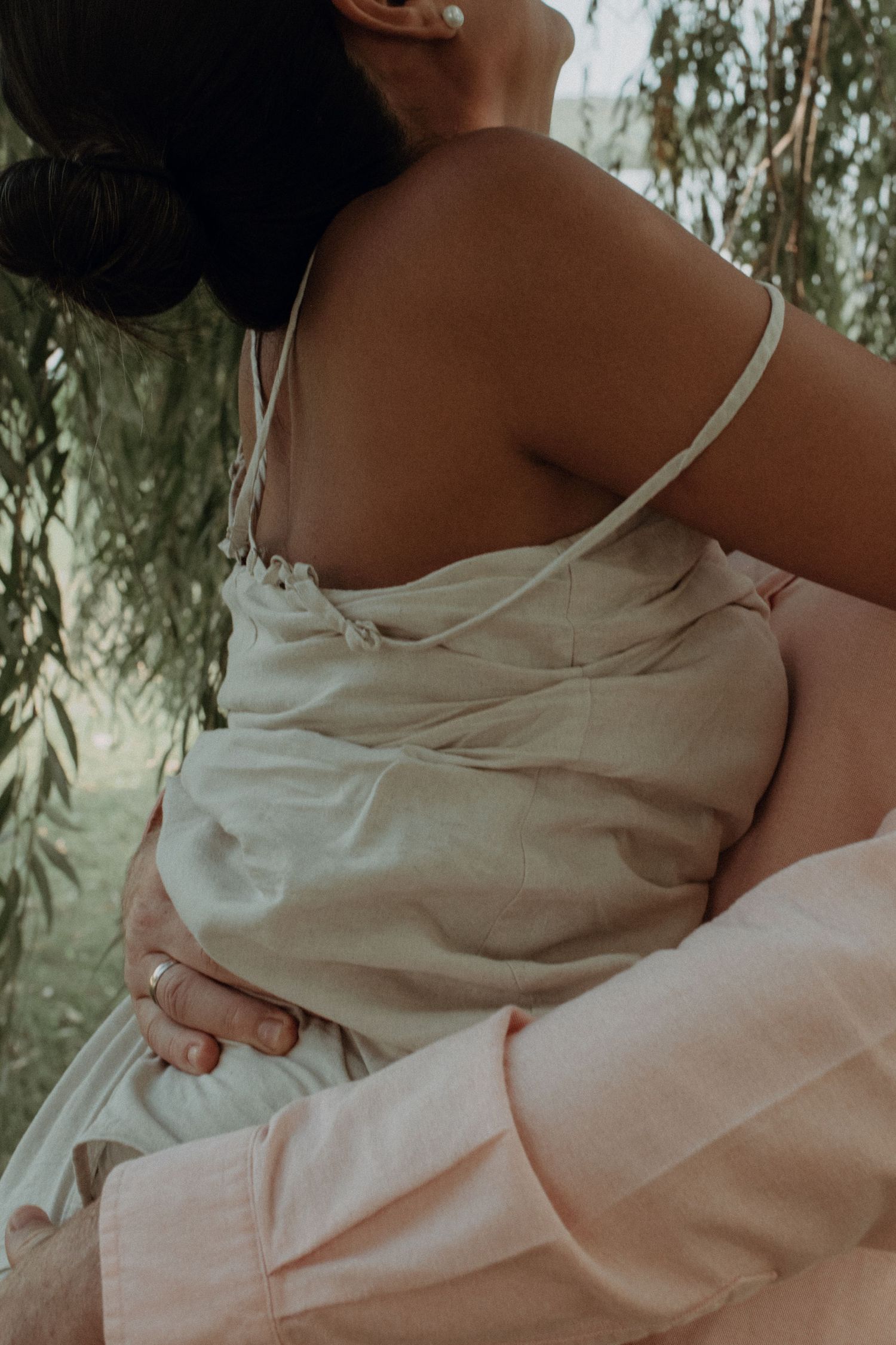 Close-up view of embracing figures wearing light colored clothing against a soft natural backdrop.
