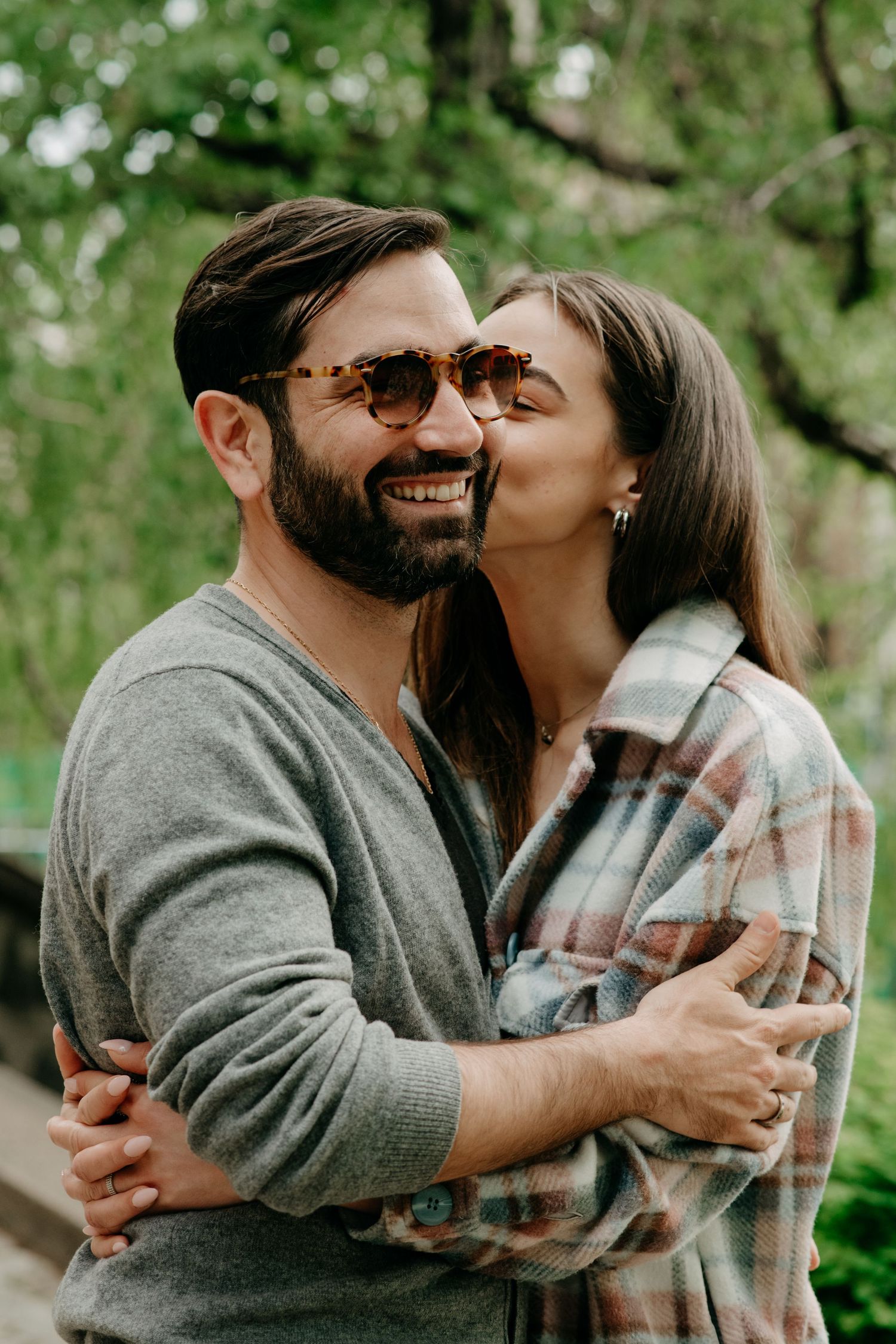 Couple sharing an affectionate embrace outdoors with natural greenery in the background.