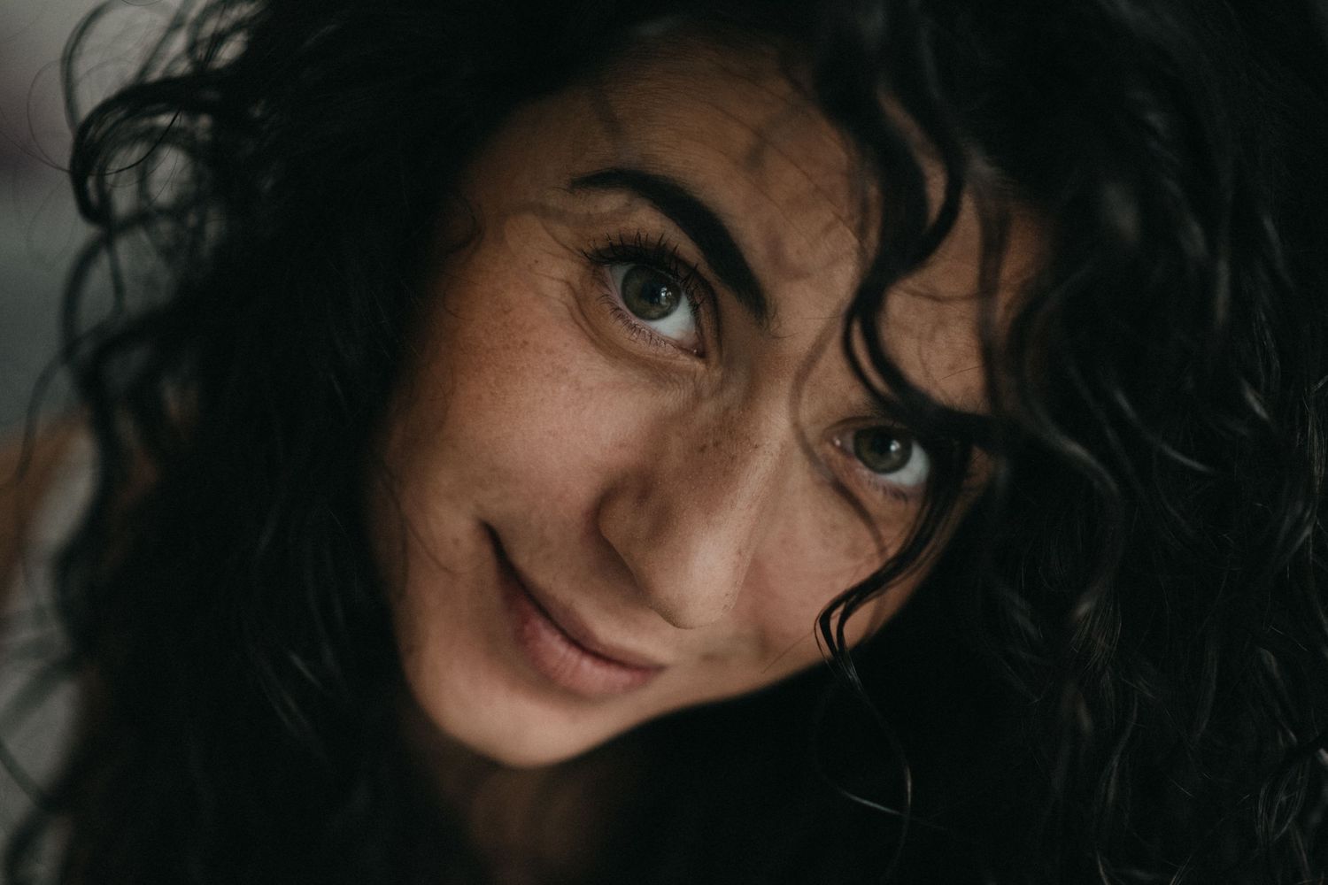 Portrait featuring dark curly hair and expressive eyes in intimate lighting.