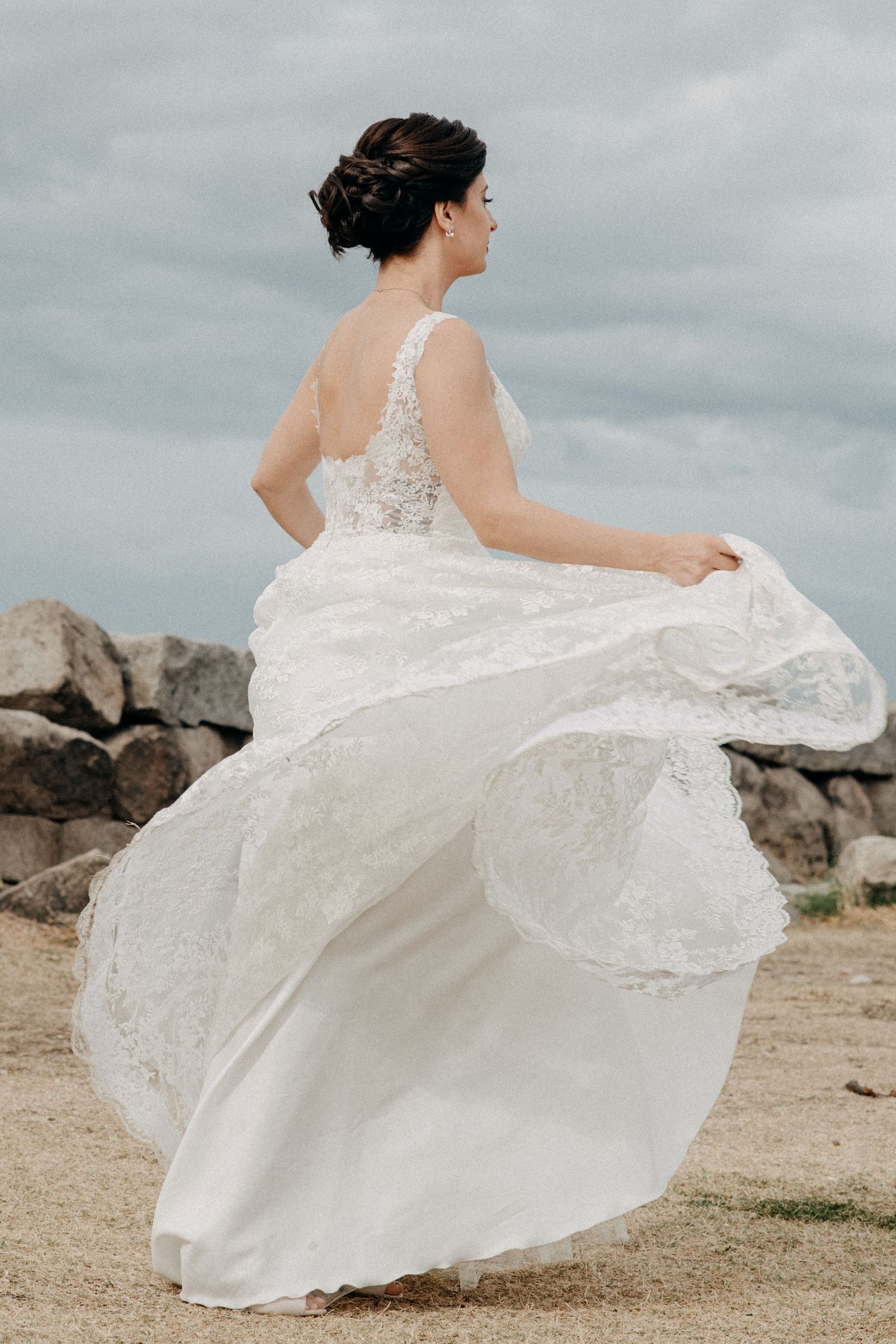 A white lace wedding dress twirling gracefully in the wind against a cloudy sky.