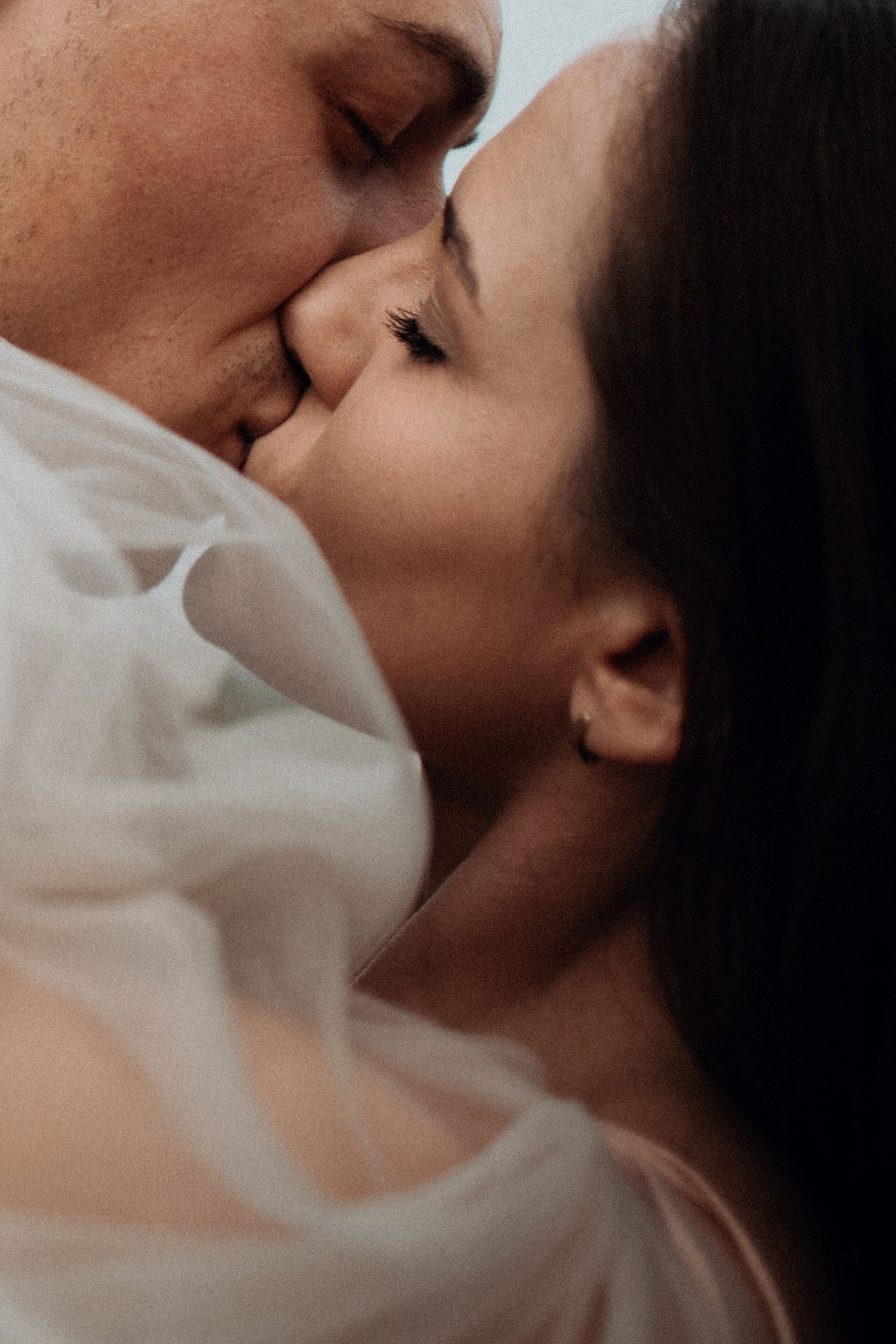 Intimate close-up of a tender kiss between newlyweds in soft lighting.