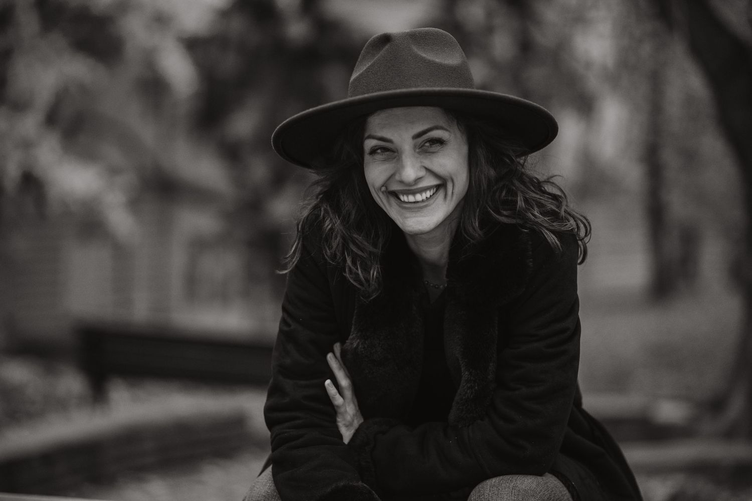 Black and white portrait of someone wearing a hat and coat outdoors in autumn.