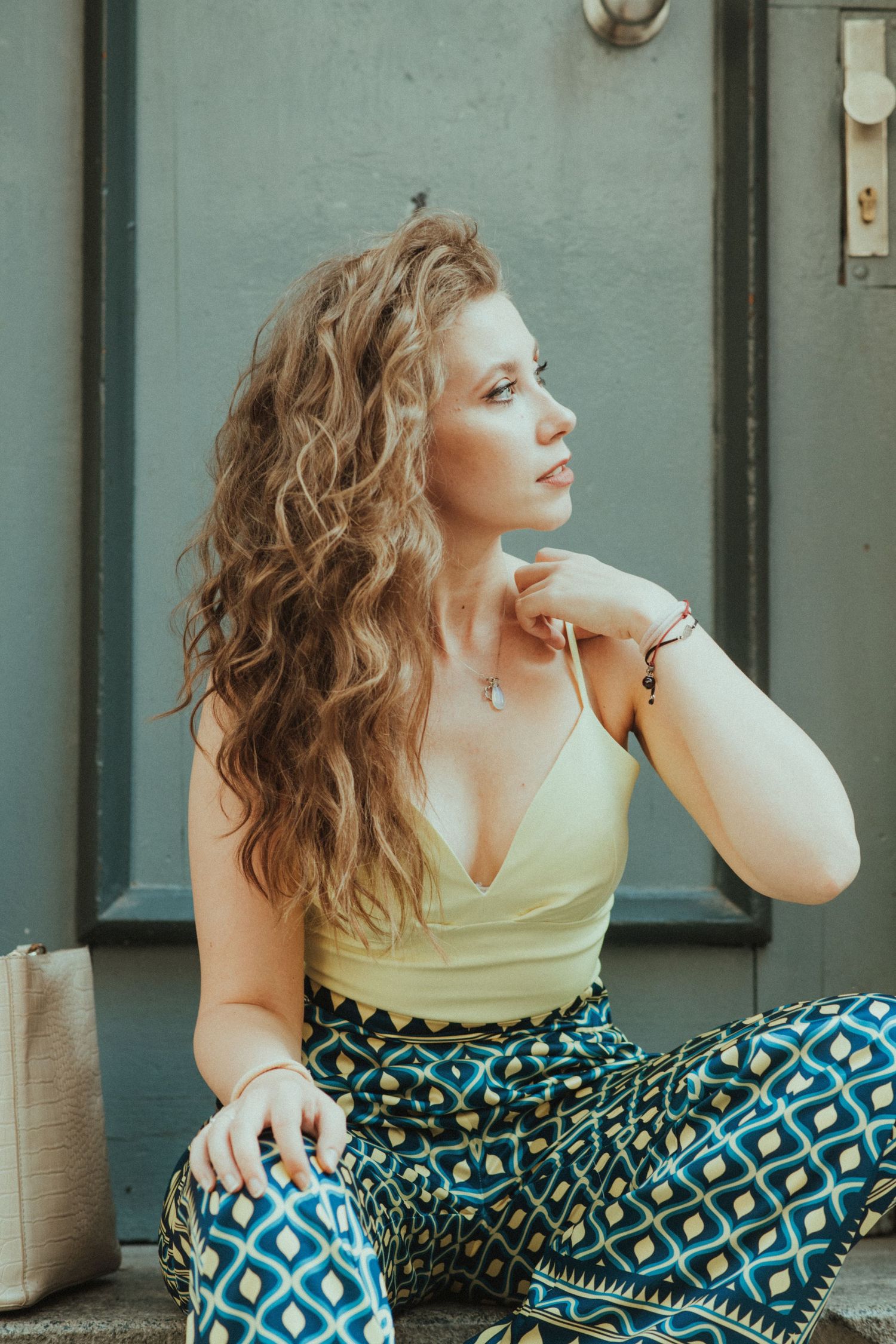 A casual portrait of someone in a yellow top and patterned pants sitting outdoors.