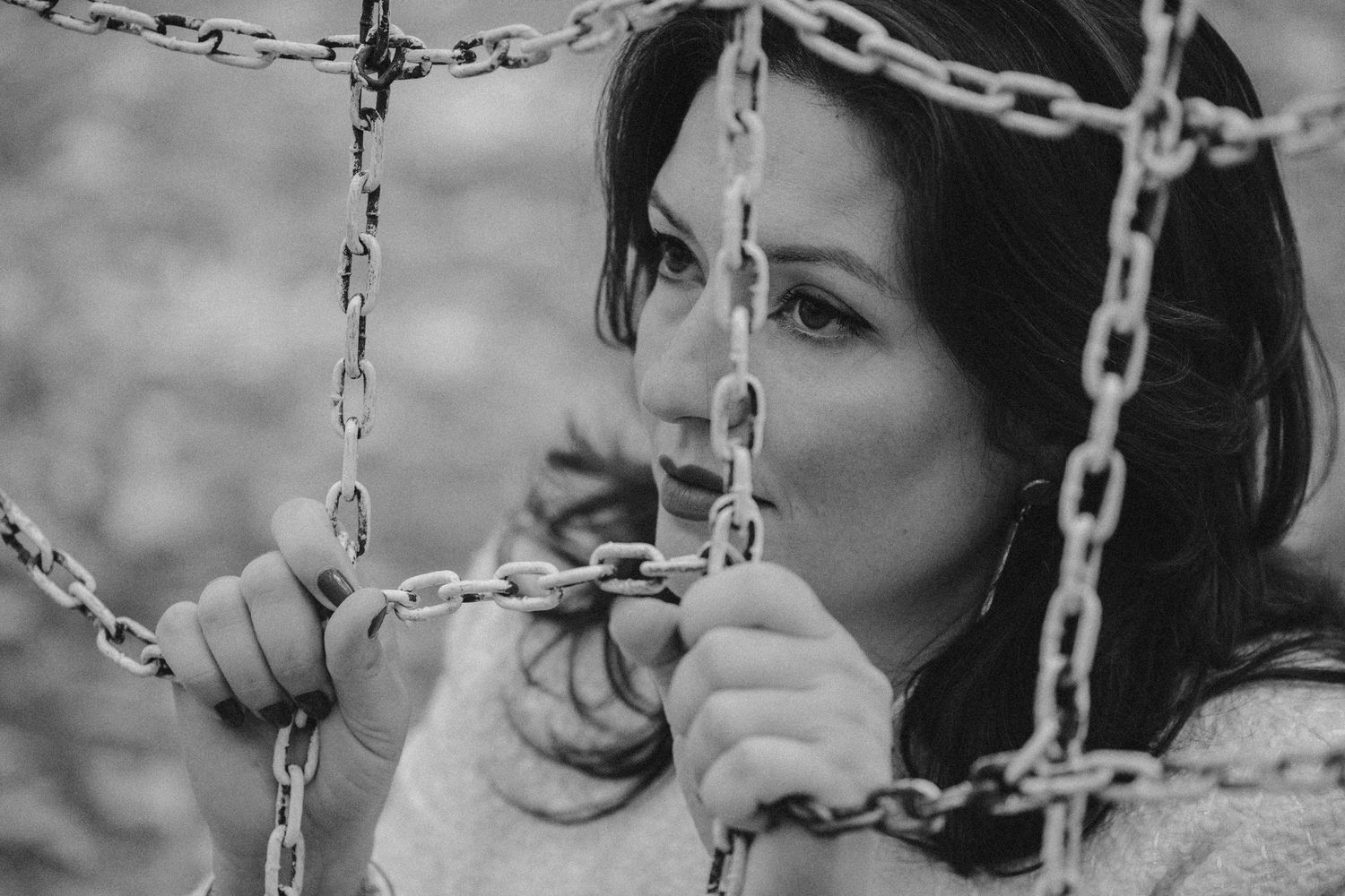 Black and white portrait of someone holding onto chain link fence with a contemplative expression.