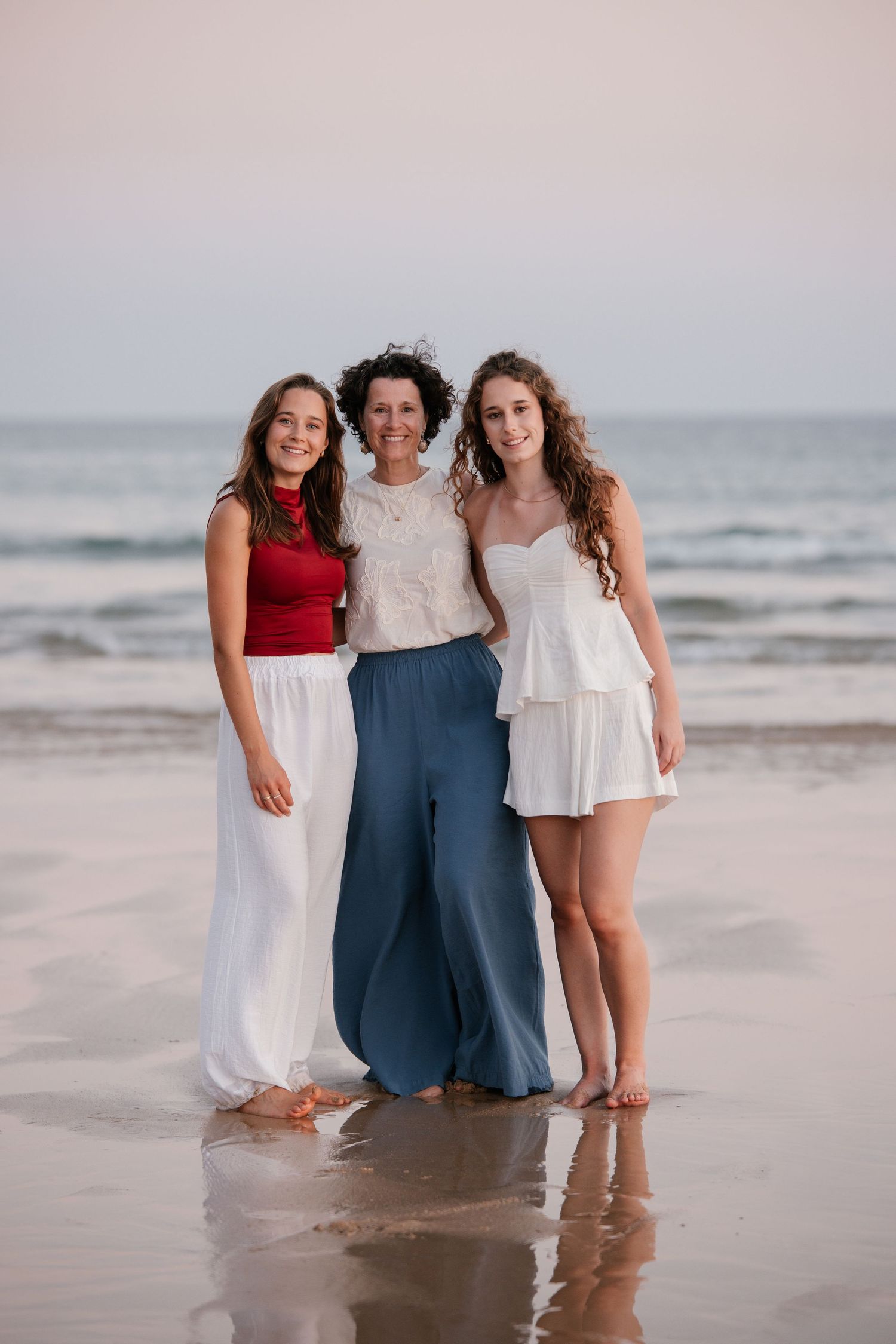 mom standing next to her two daughters on the beach during sunset, all smiling at the camera