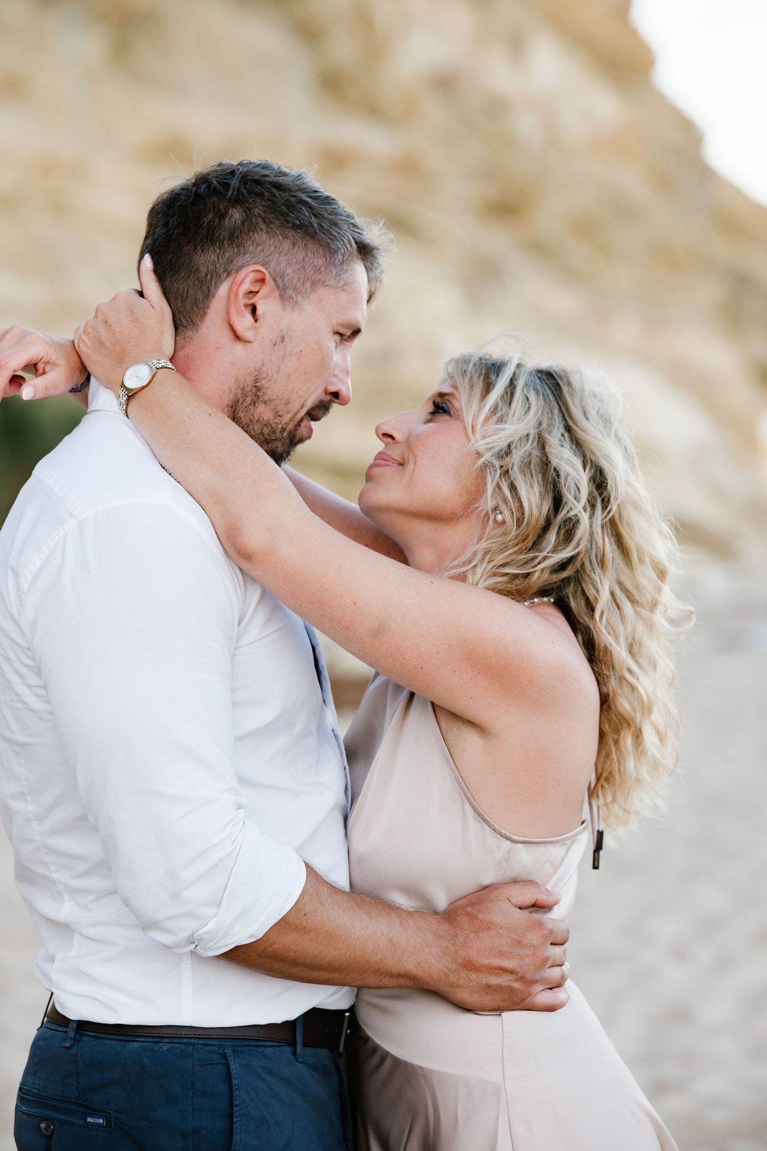 Man holding partner in his arms on sandy beach with ocean breeze blowing.