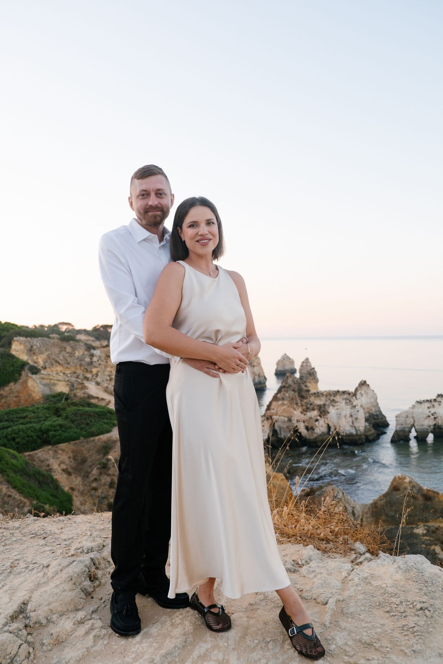 romantic couple on cliff viewpoint overlooking Três Irmãos coastline in golden morning light