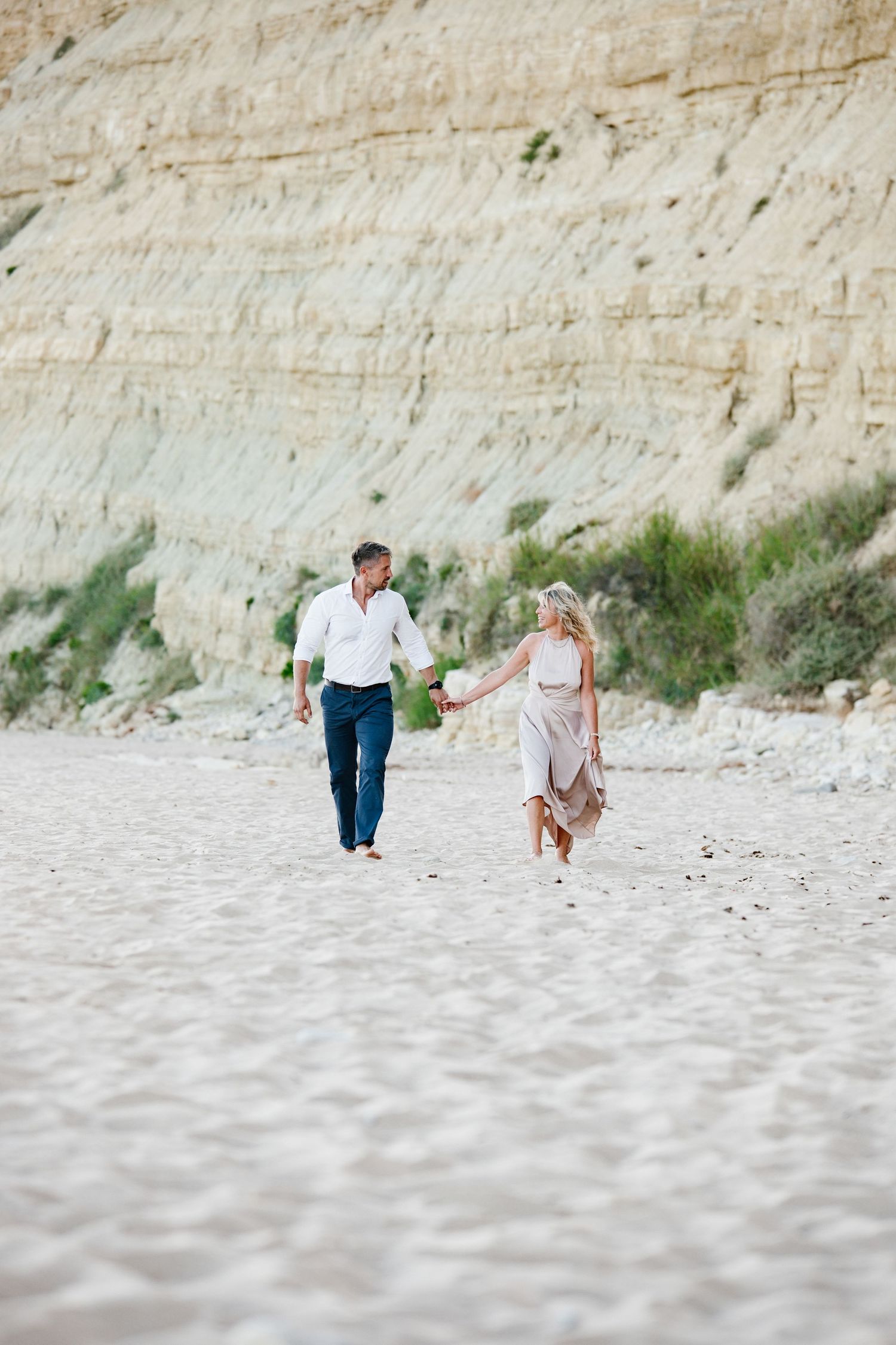 Couple walking along the shoreline at sunset with waves behind them.
