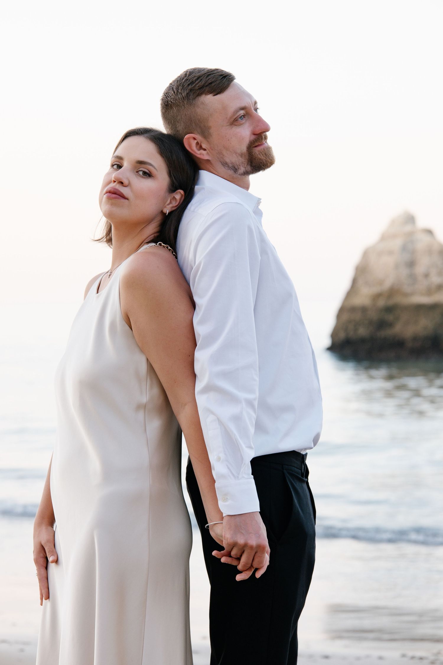 romantic standing pose of couple holding hands on Praia dos Três Irmãos with cliffs behind them