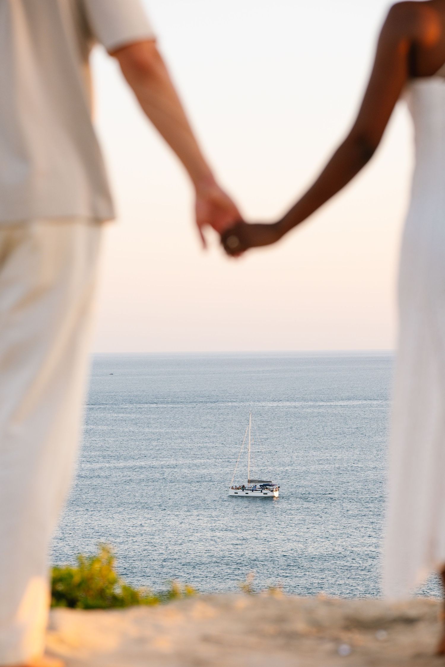 couple holding hands with the boat in the background on the ocean