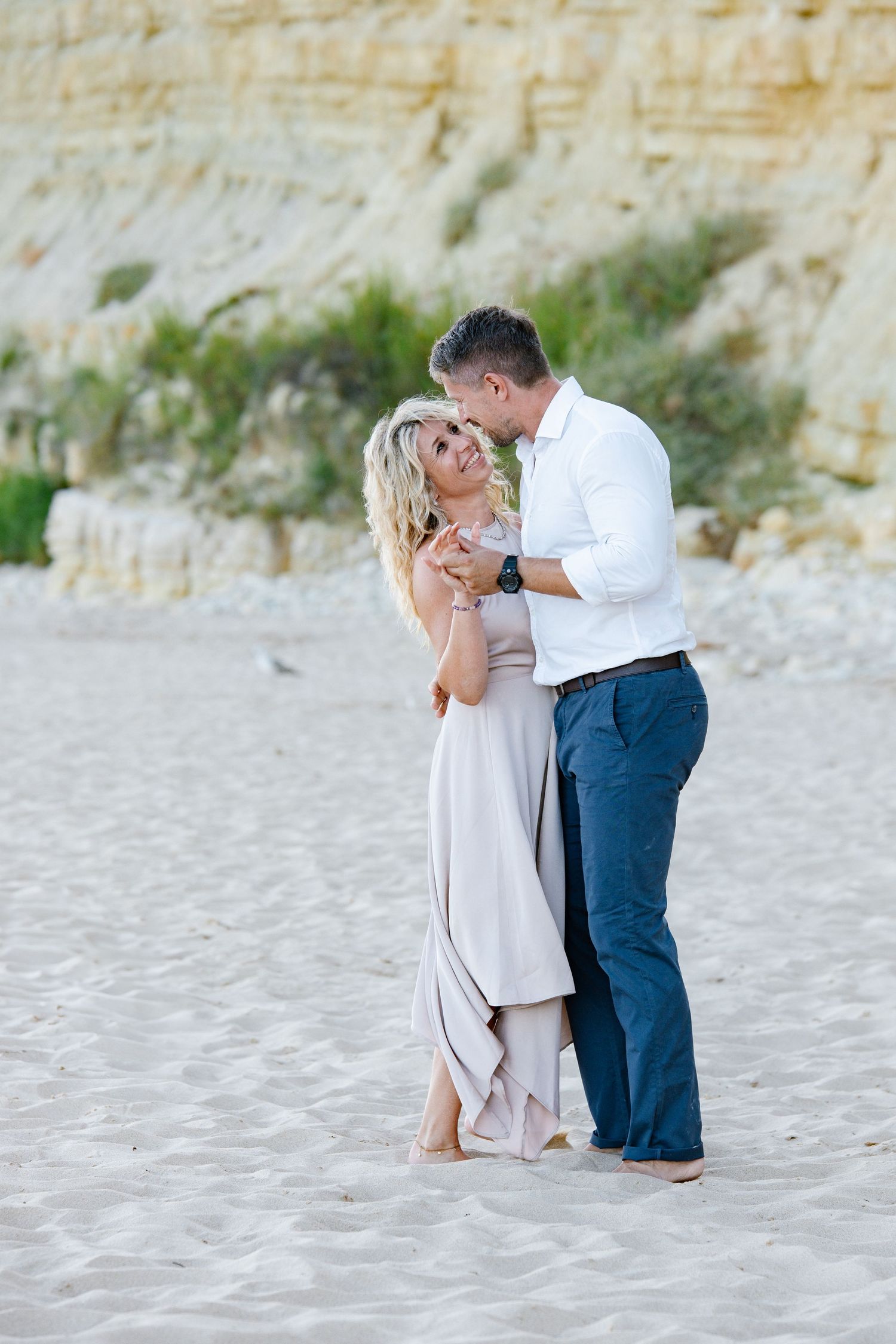 Playful moment of couple dancing barefoot on the sand with ocean breeze.