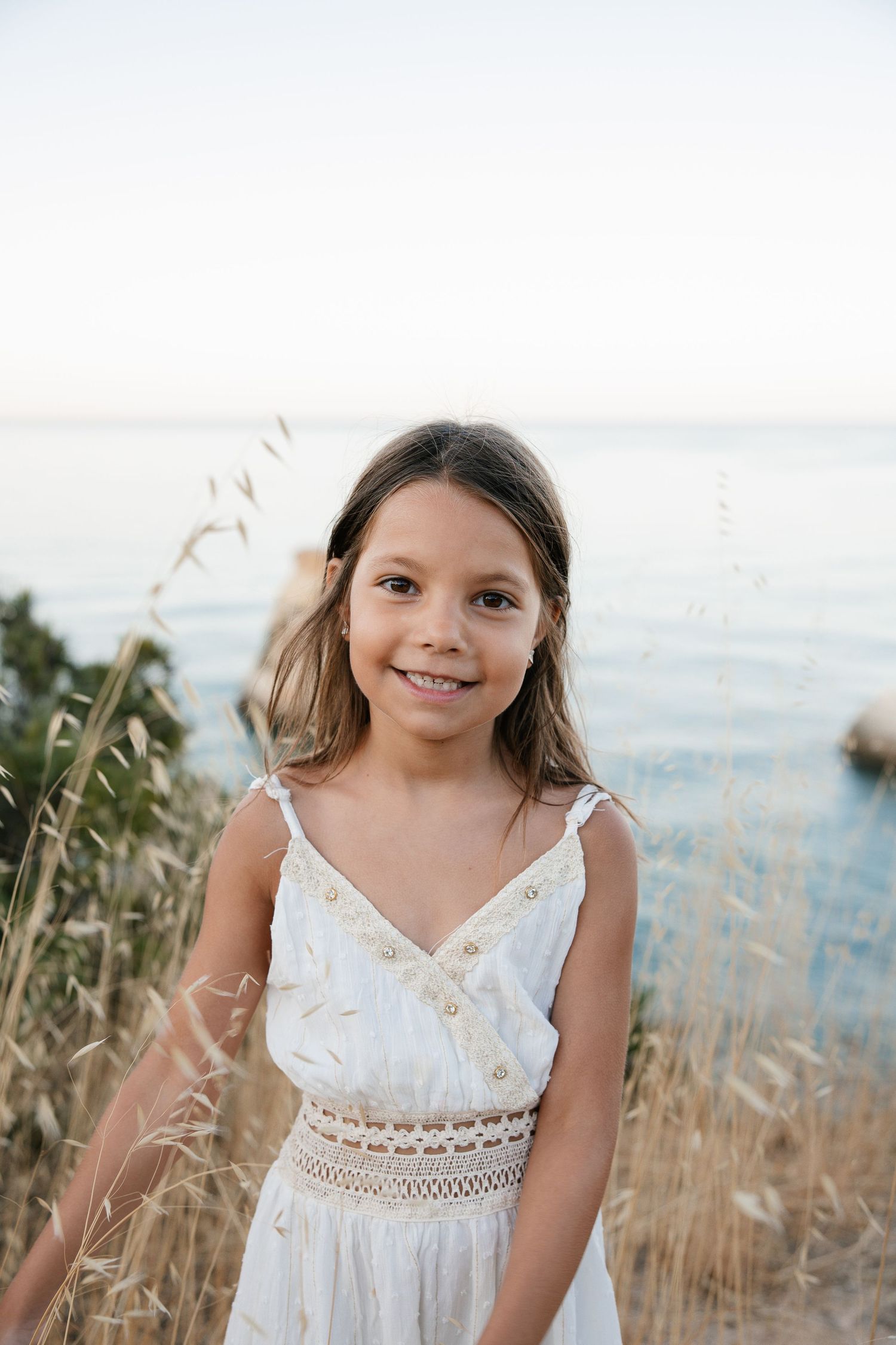 Portrait of a young girl standing on coastal cliffs with ocean views behind her.