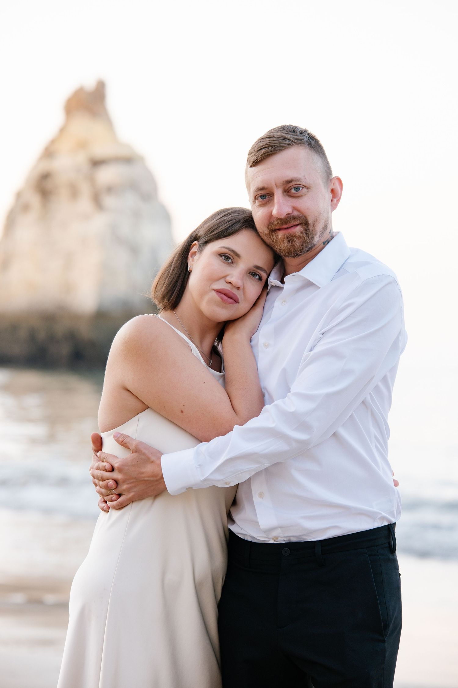 Romantic sunrise portrait of couple standing between rock formations at Três Irmãos beach Algarve