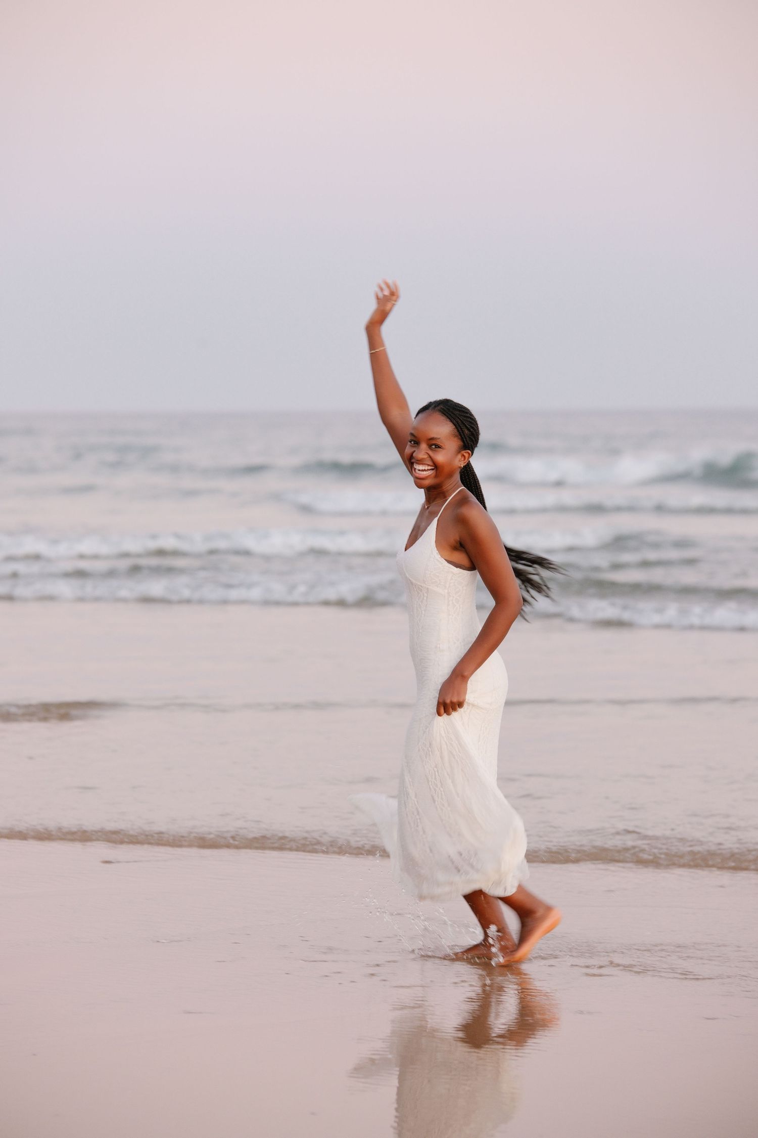 Black woman with white dress running on the beach with waves in the background