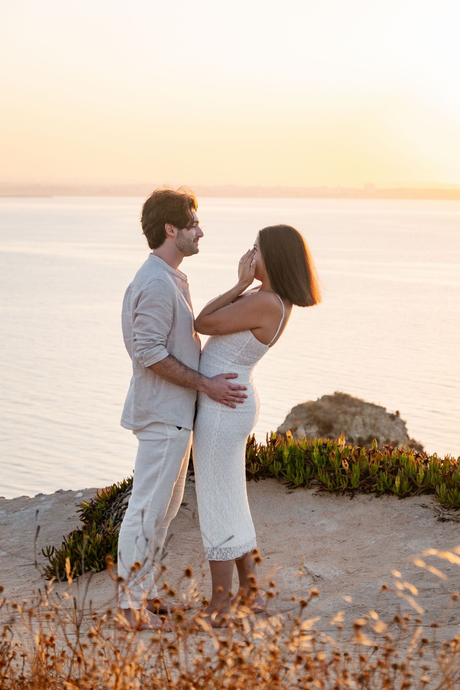 emotional engagement moment on cliffs with Praia da Camilo rock stacks glowing in sunrise light — proposal photography Algarve
