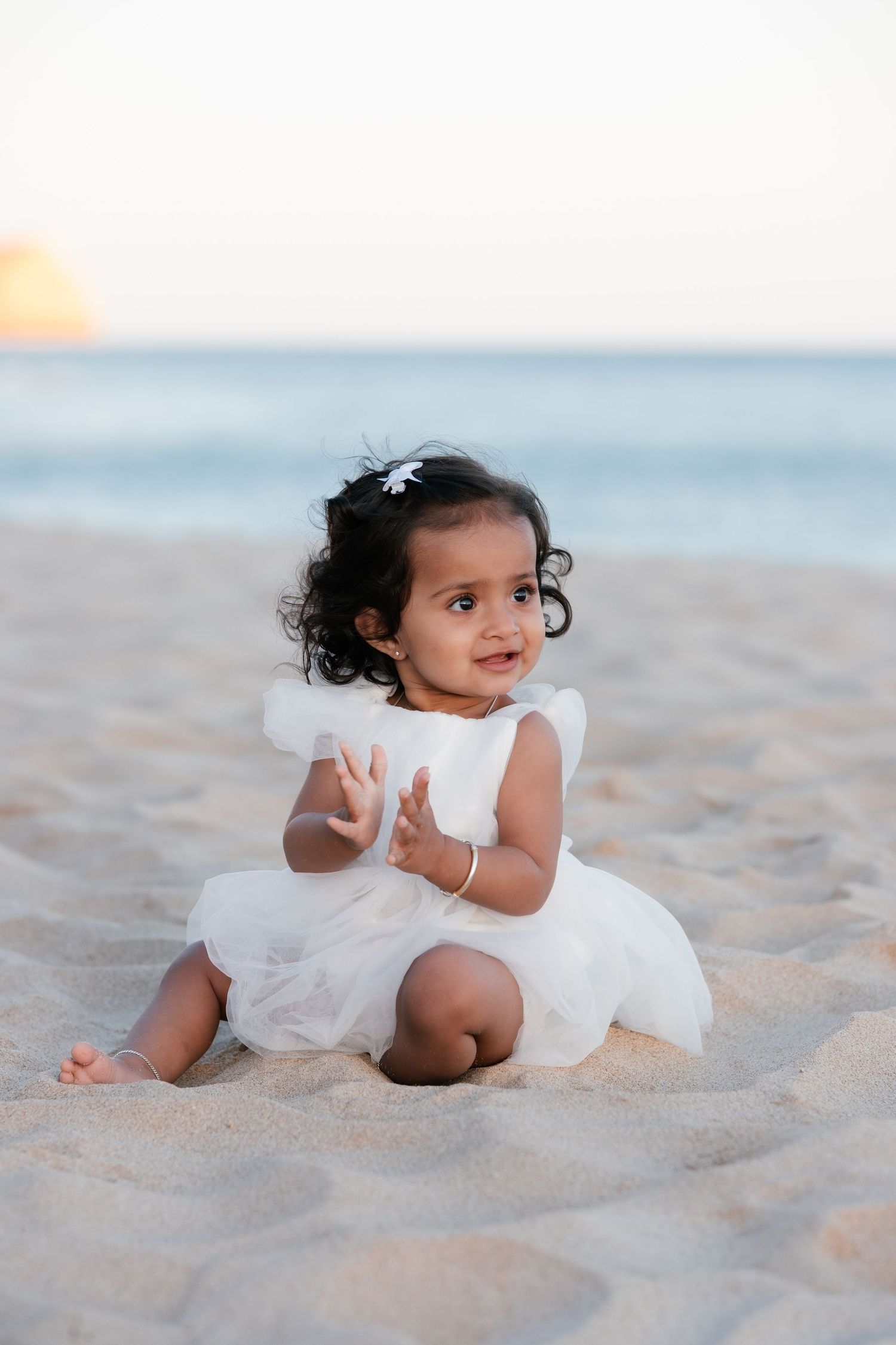 baby playing in sand with gentle waves behind during first birthday photoshoot in the Algarve