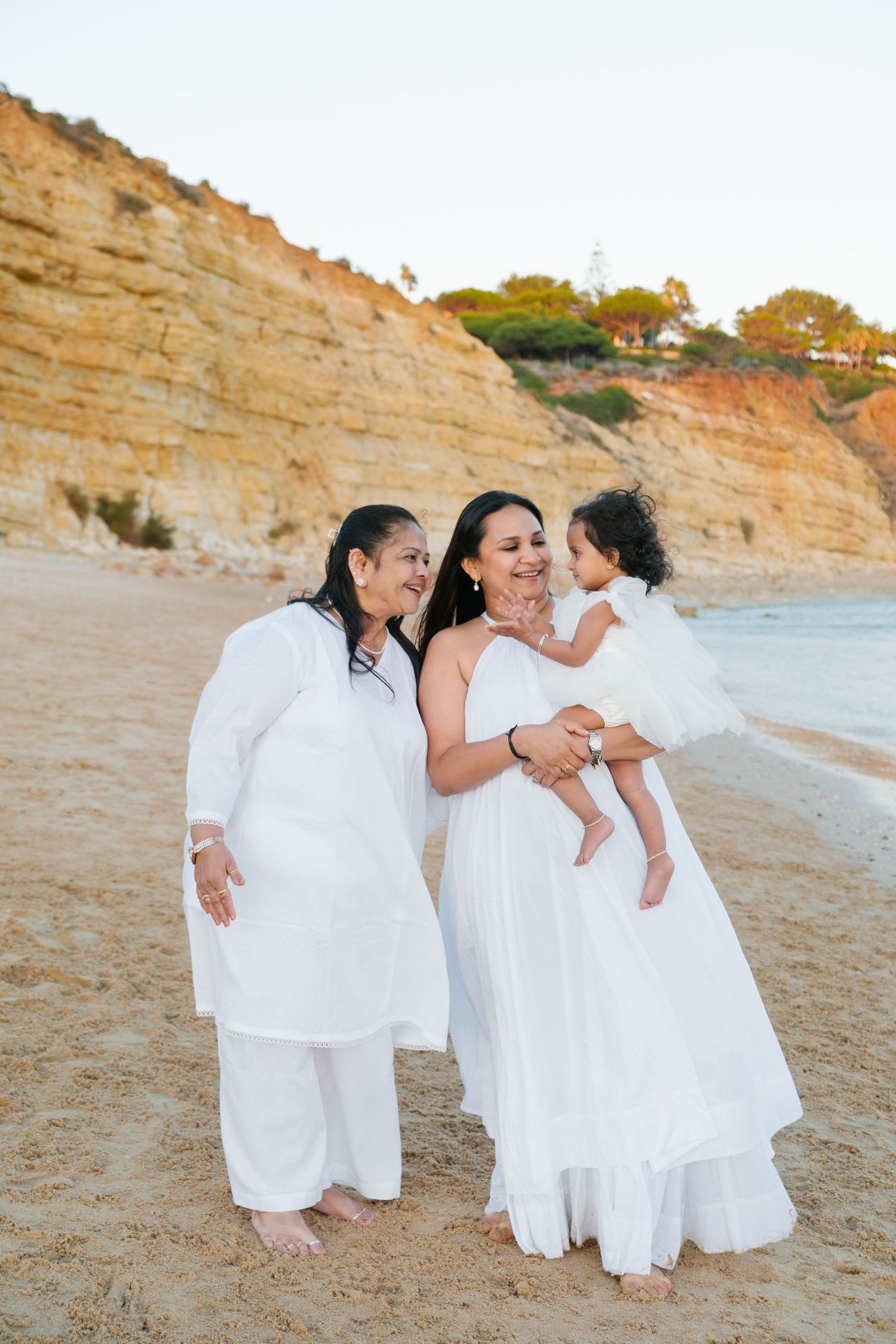 parents holding their baby between them while walking along Porto de Mós beach at sunset