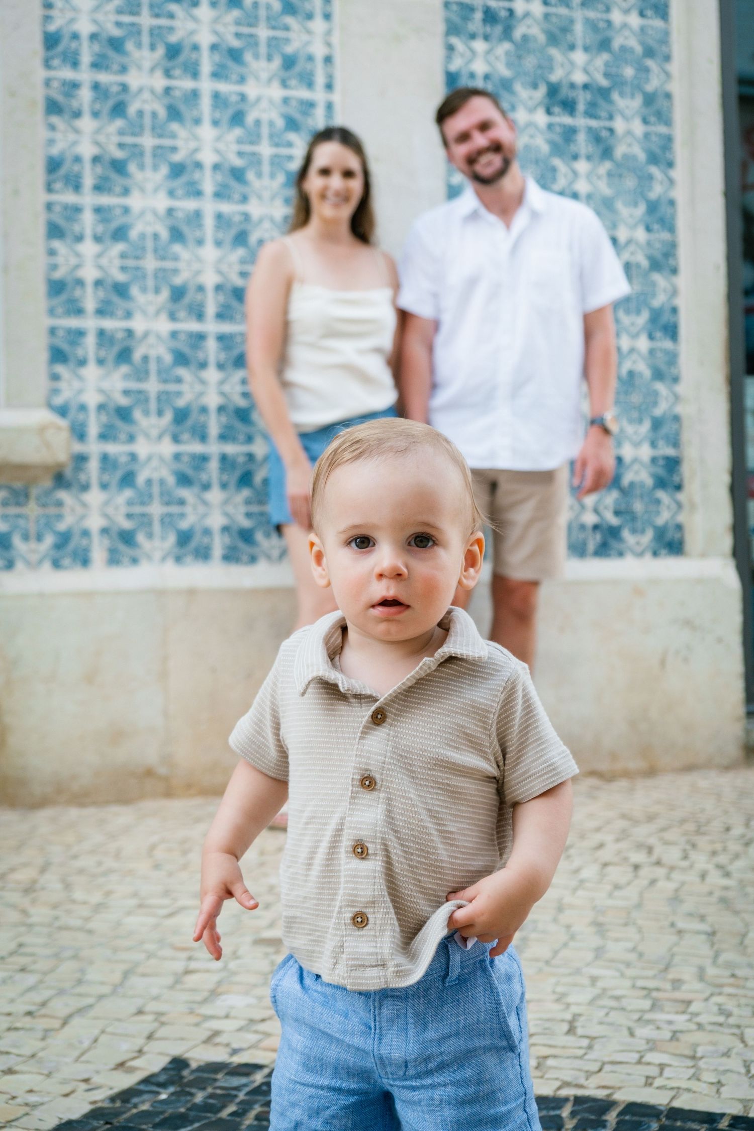 toddler making a funny pose in a charming Algarve street while parents smile in the background