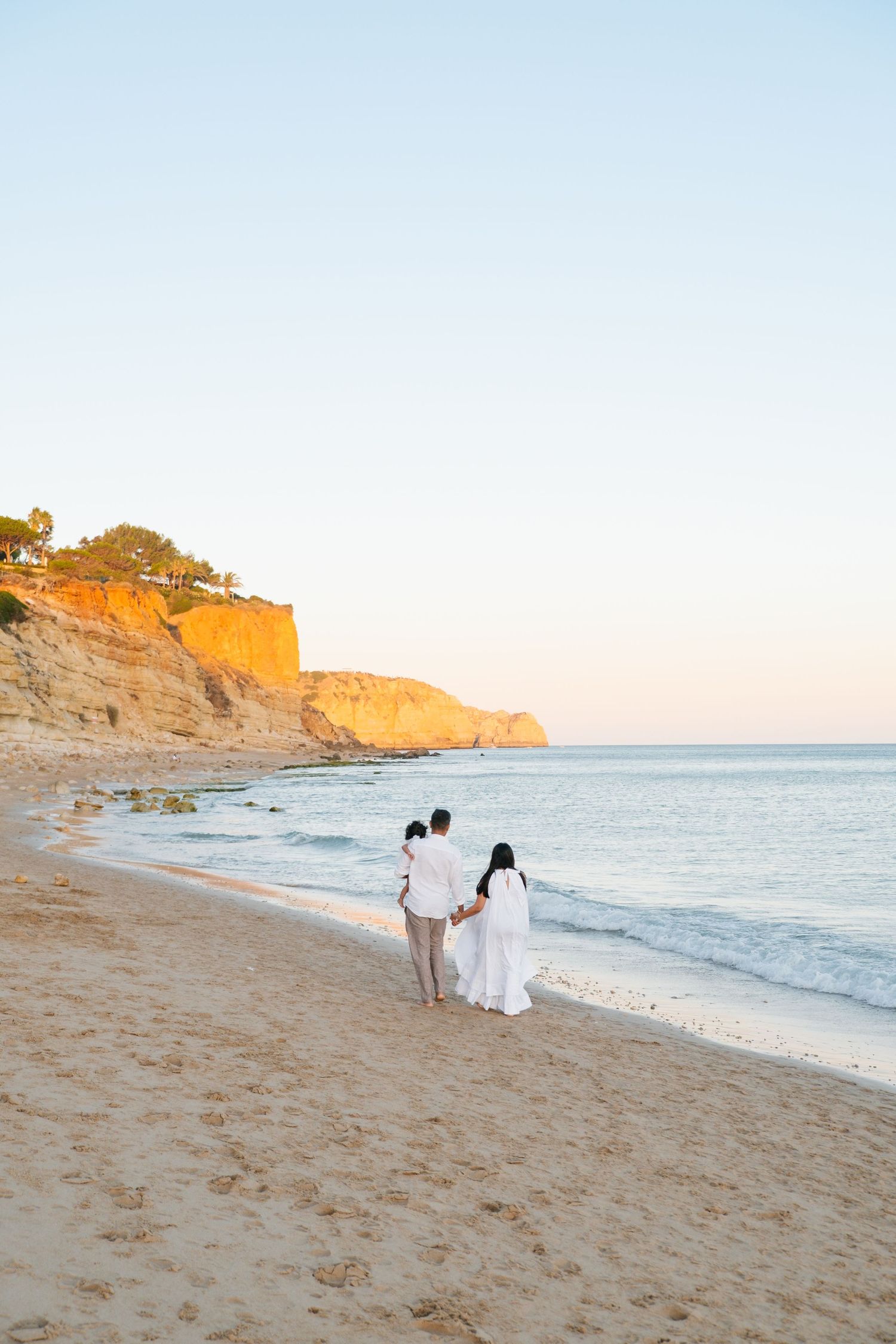 portrait of family walking toward cliffs at Porto de Mós during golden hour first birthday shoot