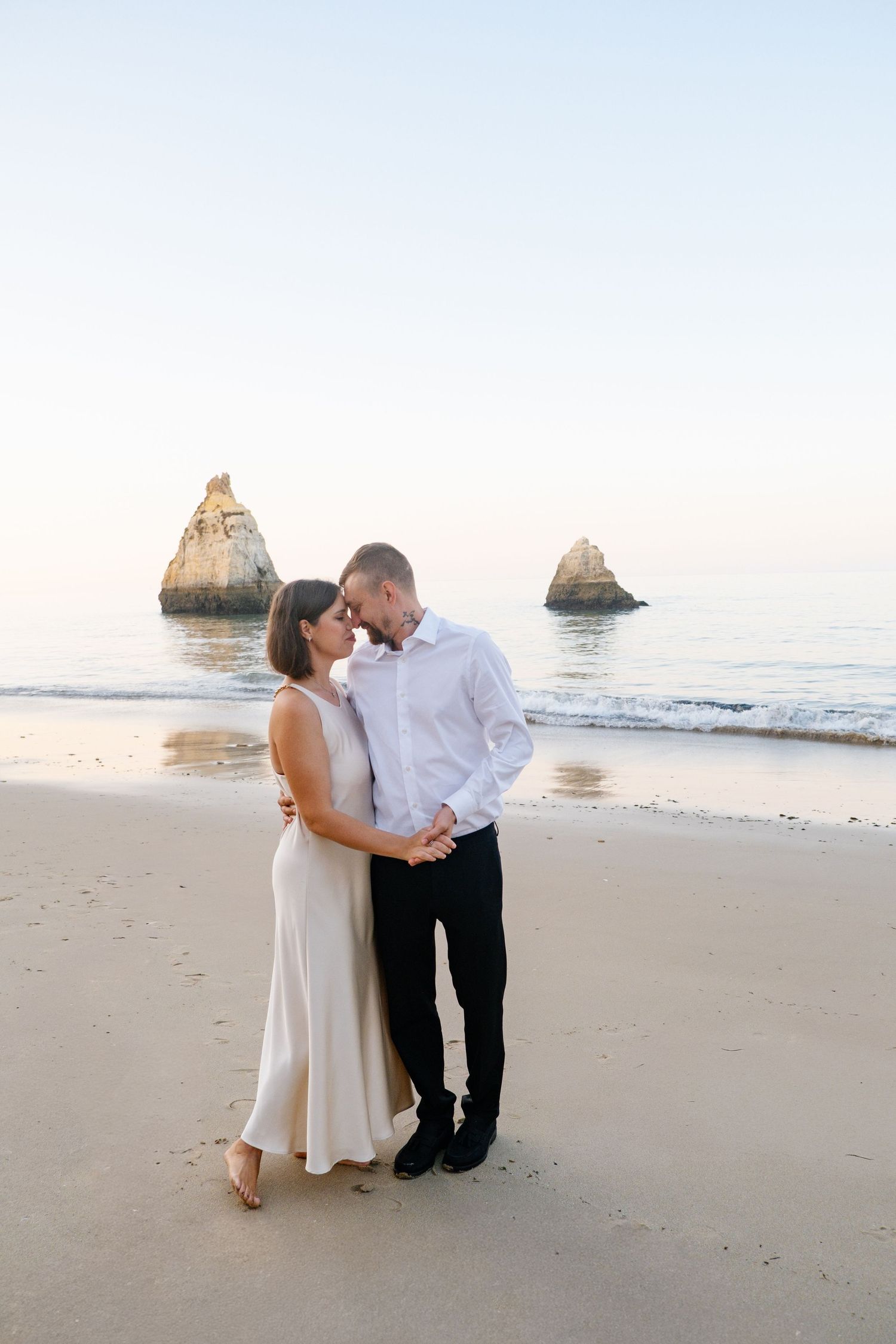 couple walking along Praia dos Três Irmãos at sunrise with cliffs glowing in soft light