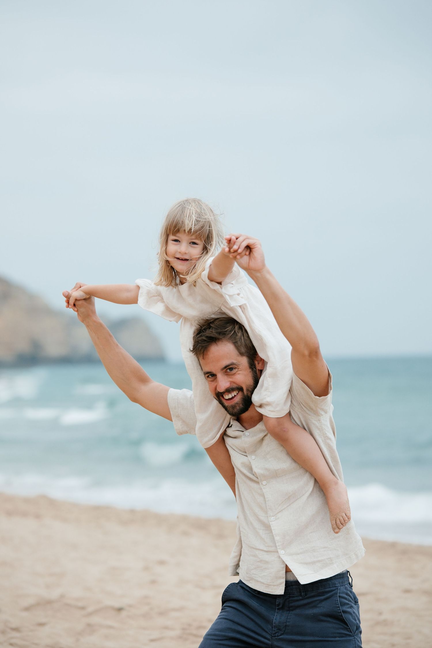 Father lifting daughter by the ocean at Porto Mós with sunrise light on Algarve cliffs.