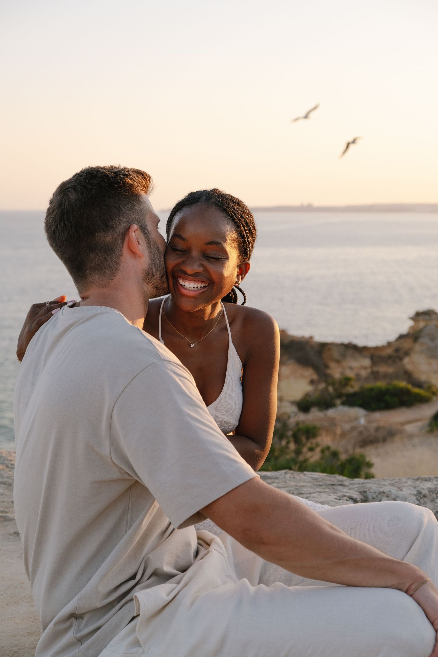 man kisses his girlfriend with birds and ocean of portugal in the background