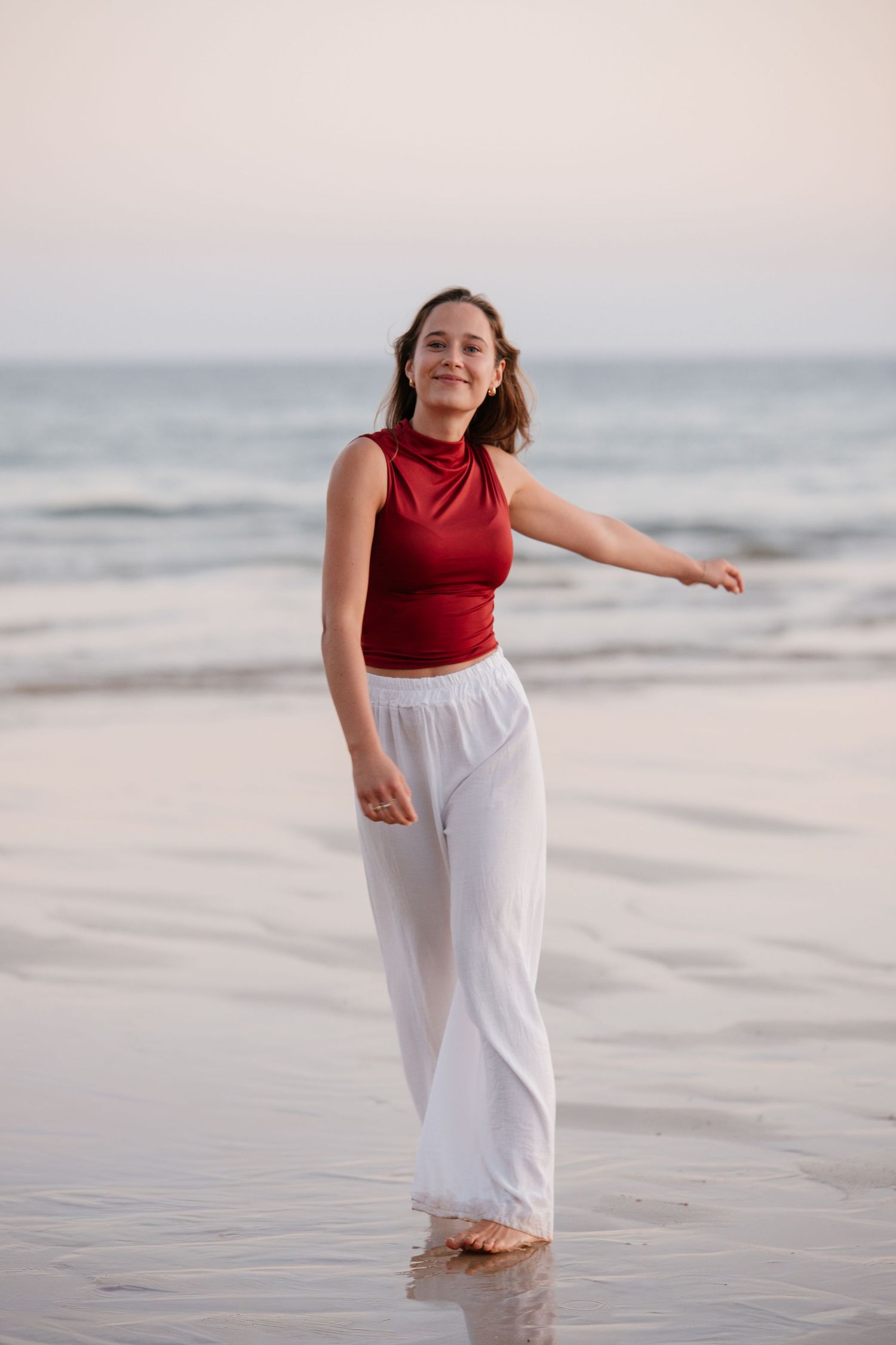 girl walking on wet sand at sunset in red shirt and white pants near Alvor