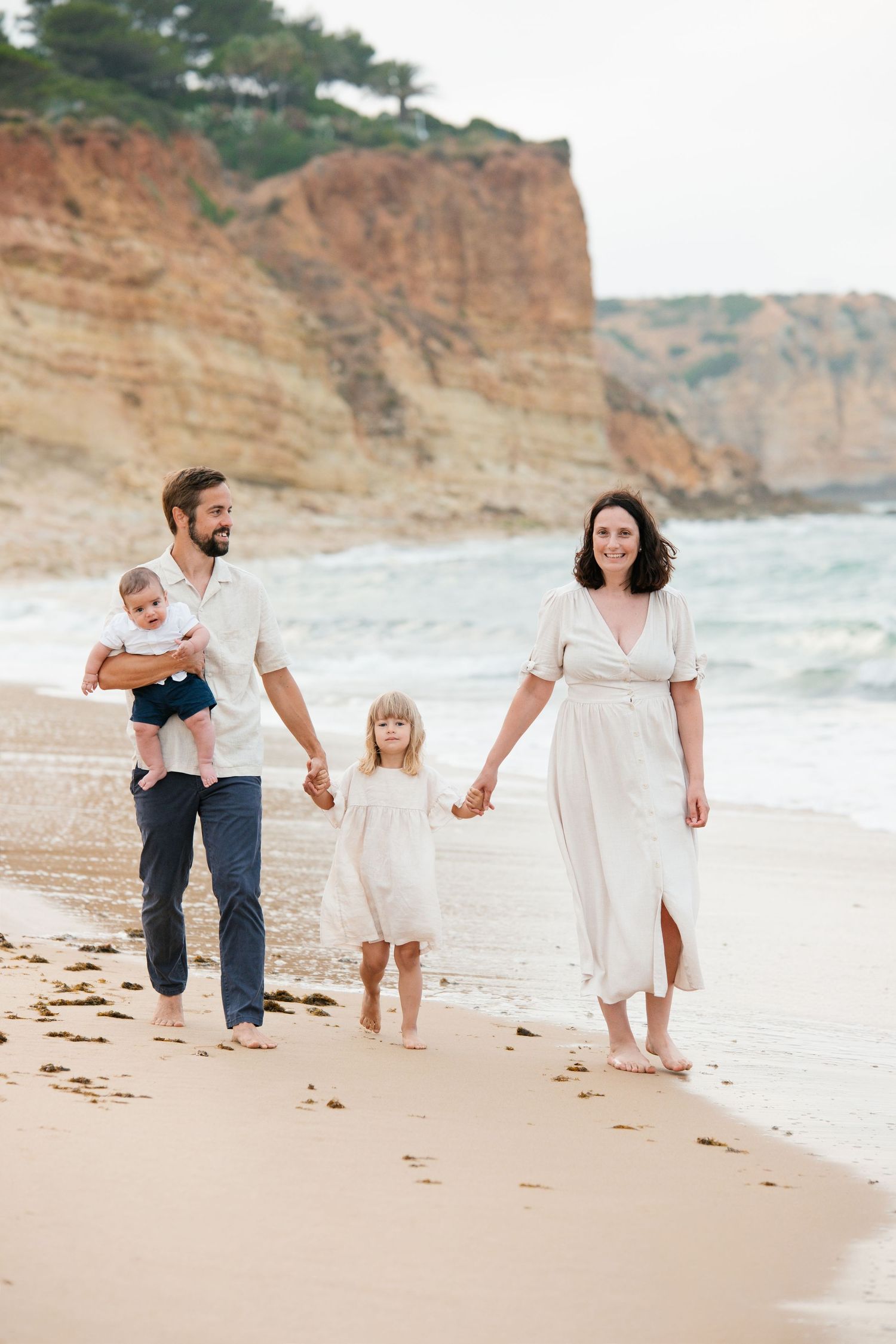 Parents and kids walking on sandy shoreline with morning light in Algarve, Portugal.