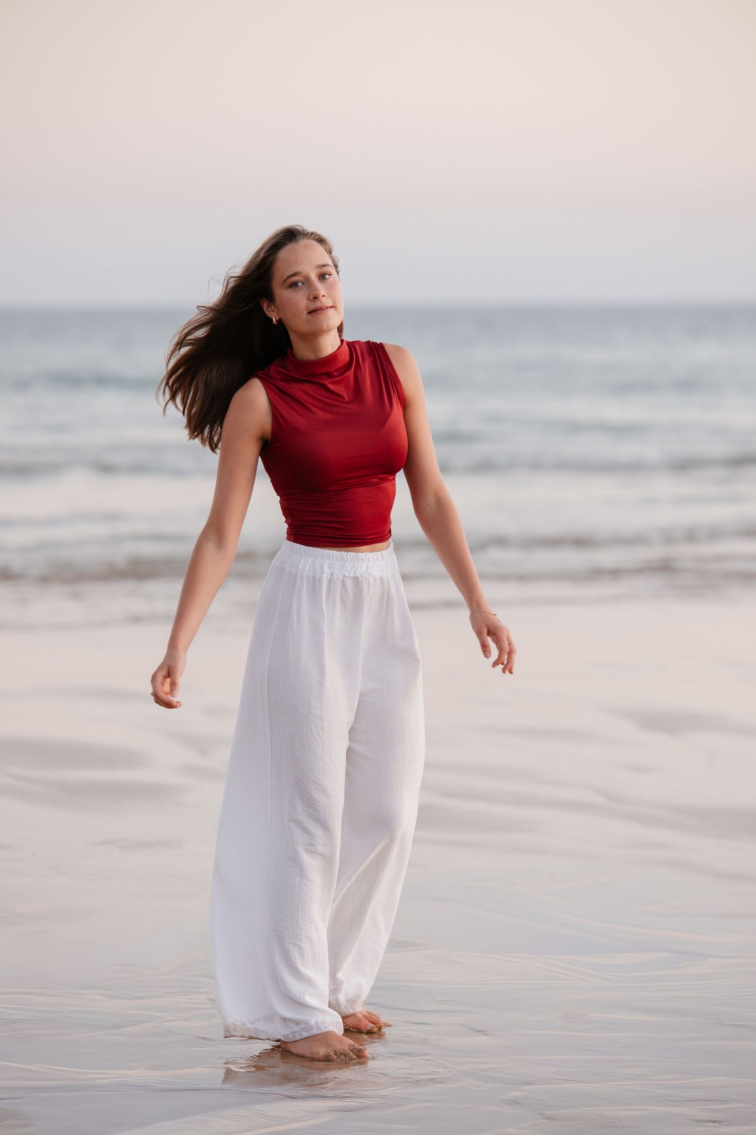 soft golden sunset portrait of girl standing by shoreline at Praia Três Irmãos wearing red top and white pants