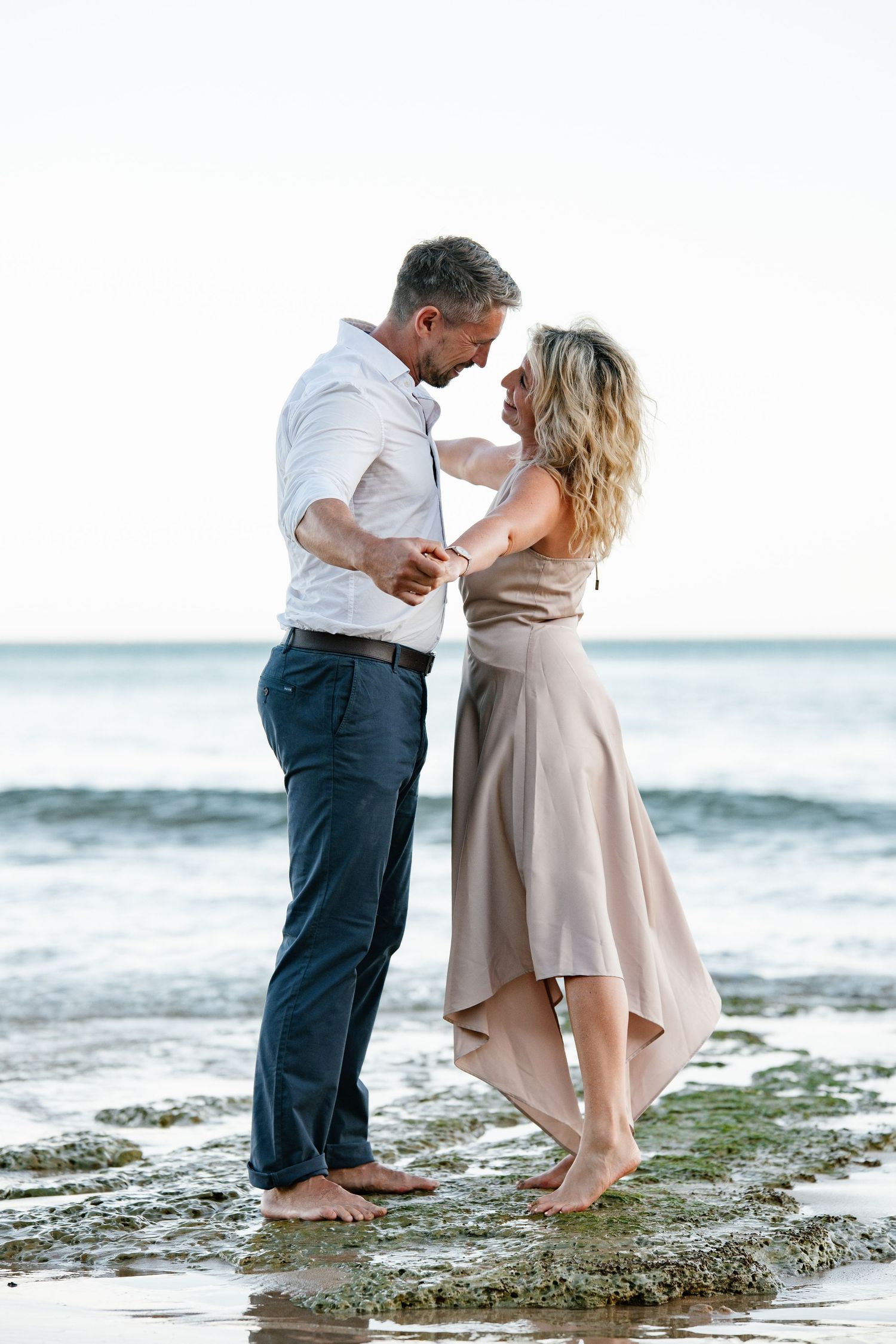 Couple standing close together on the shoreline with waves reaching their feet.