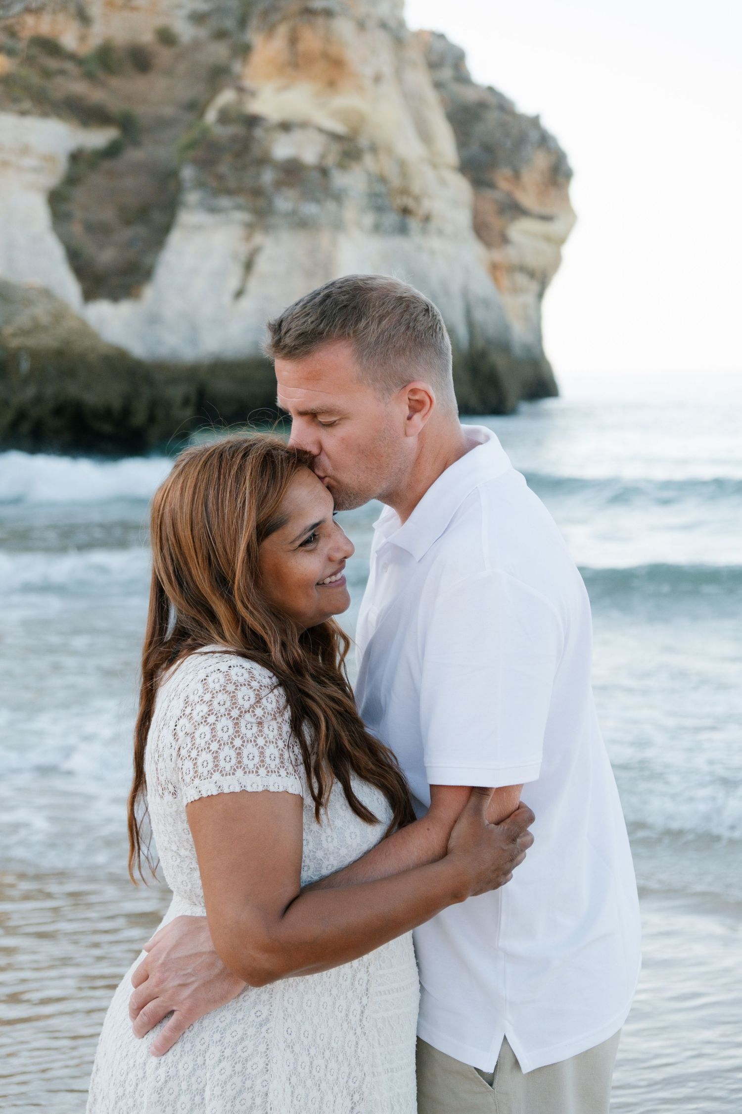 Parents sharing a kiss on the beach with soft natural light.