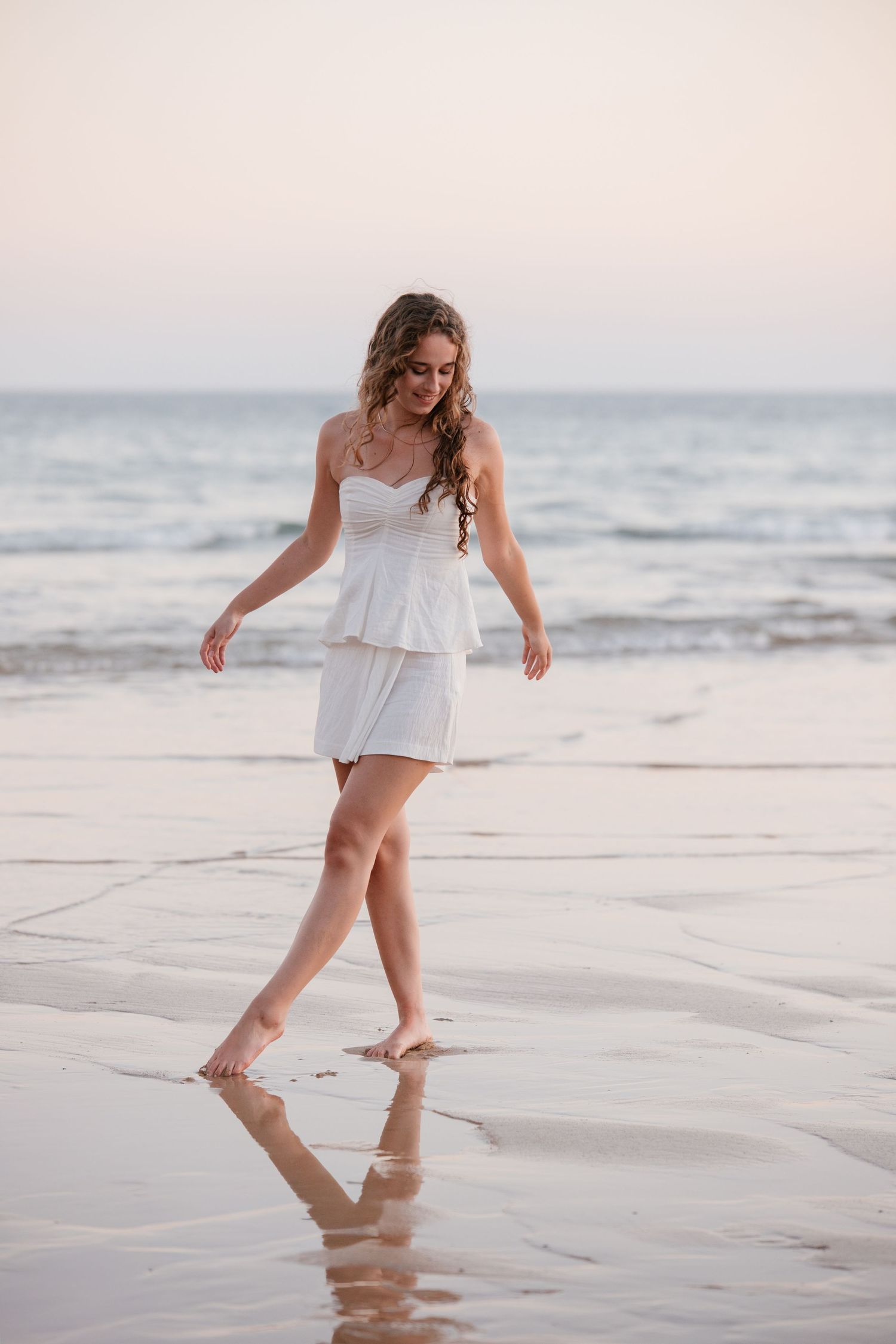 playful close-up portrait of girl wearing a white dress on beach in Algarve during sunset