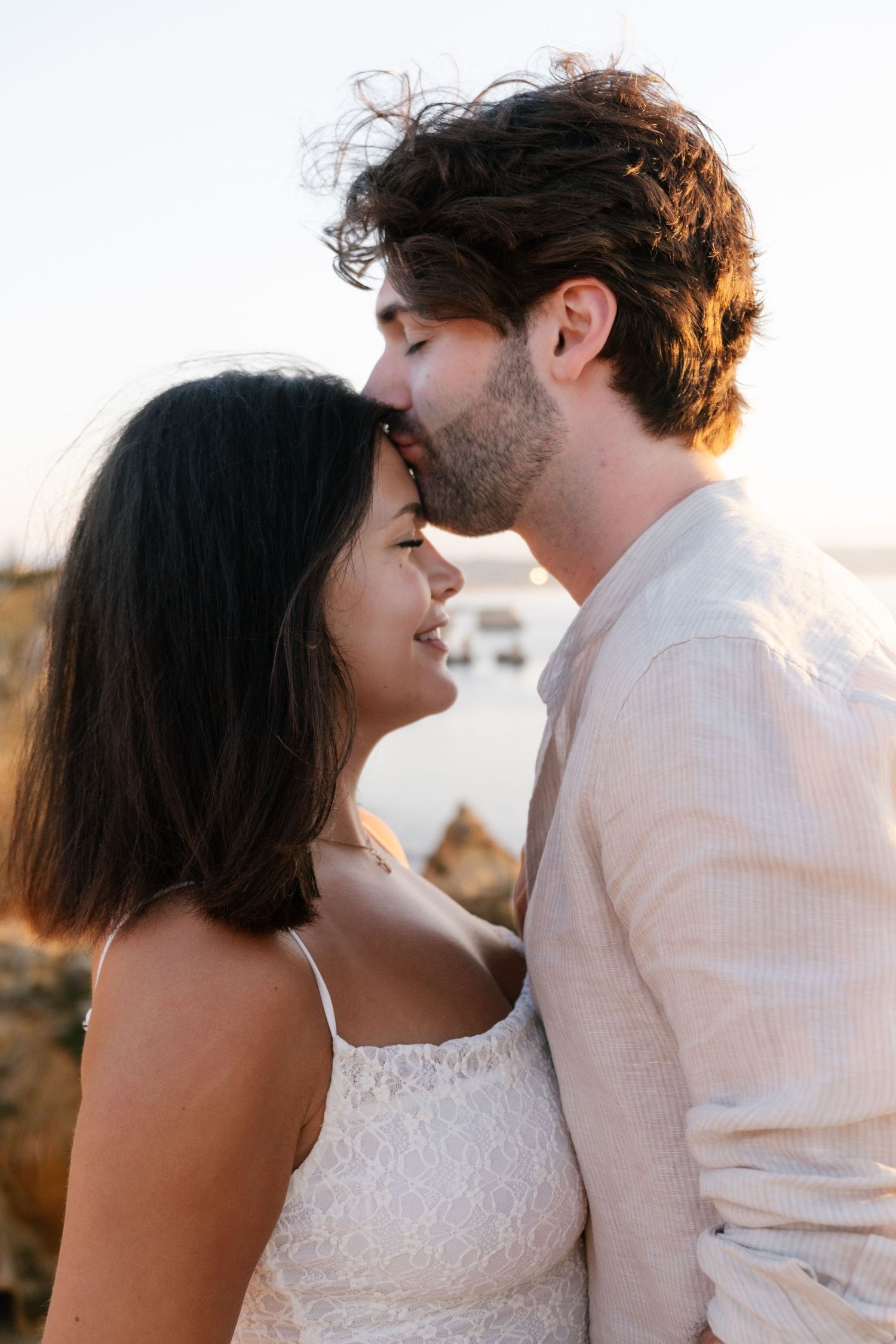 emotional engagement moment on cliffs with Praia da Camilo rock stacks glowing in sunrise light